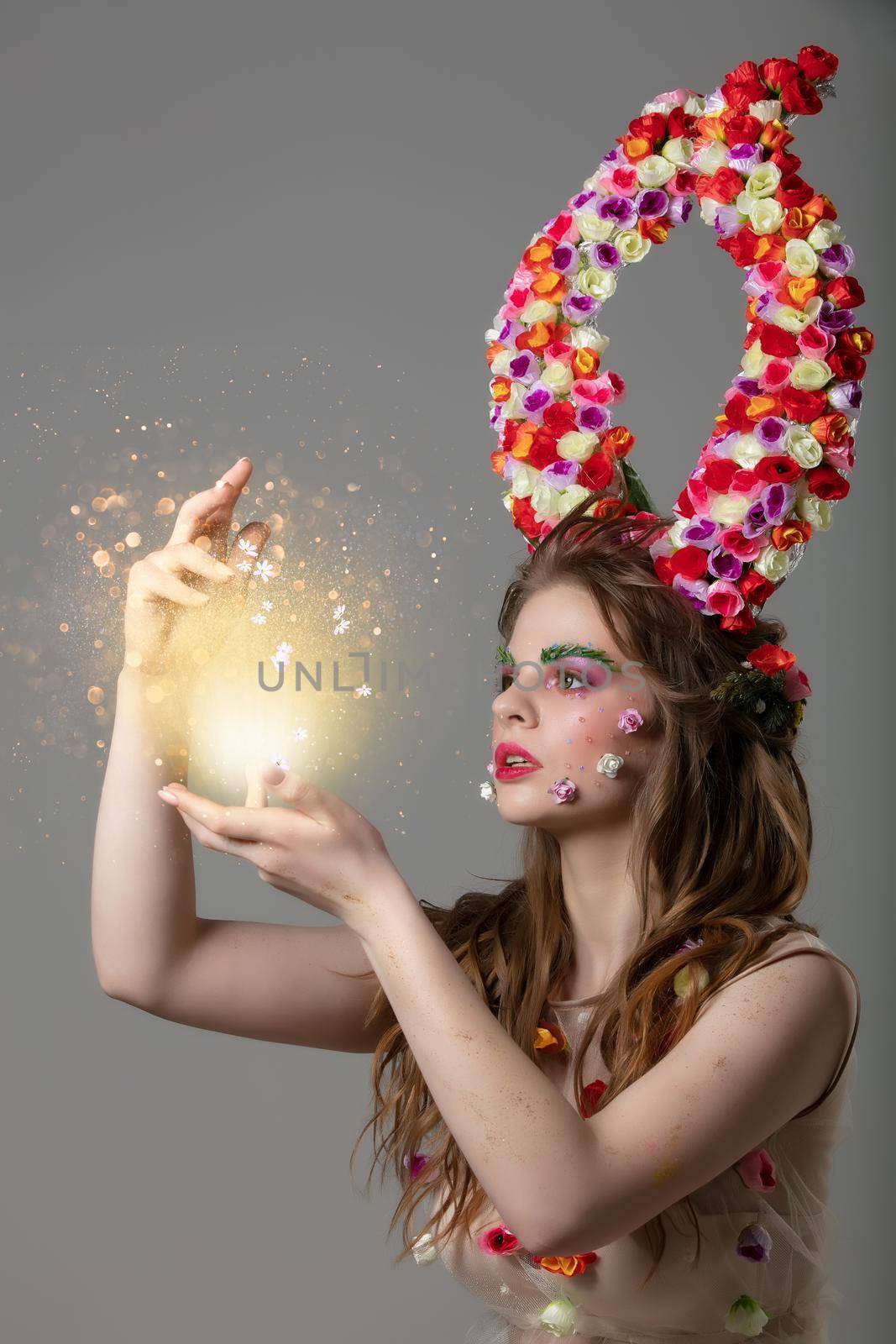 A fabulous girl with floral horns and fantastic make-up holds a glowing ball. Spring or summer beauty. Fantastic woman.Goddess of flowers Flora.