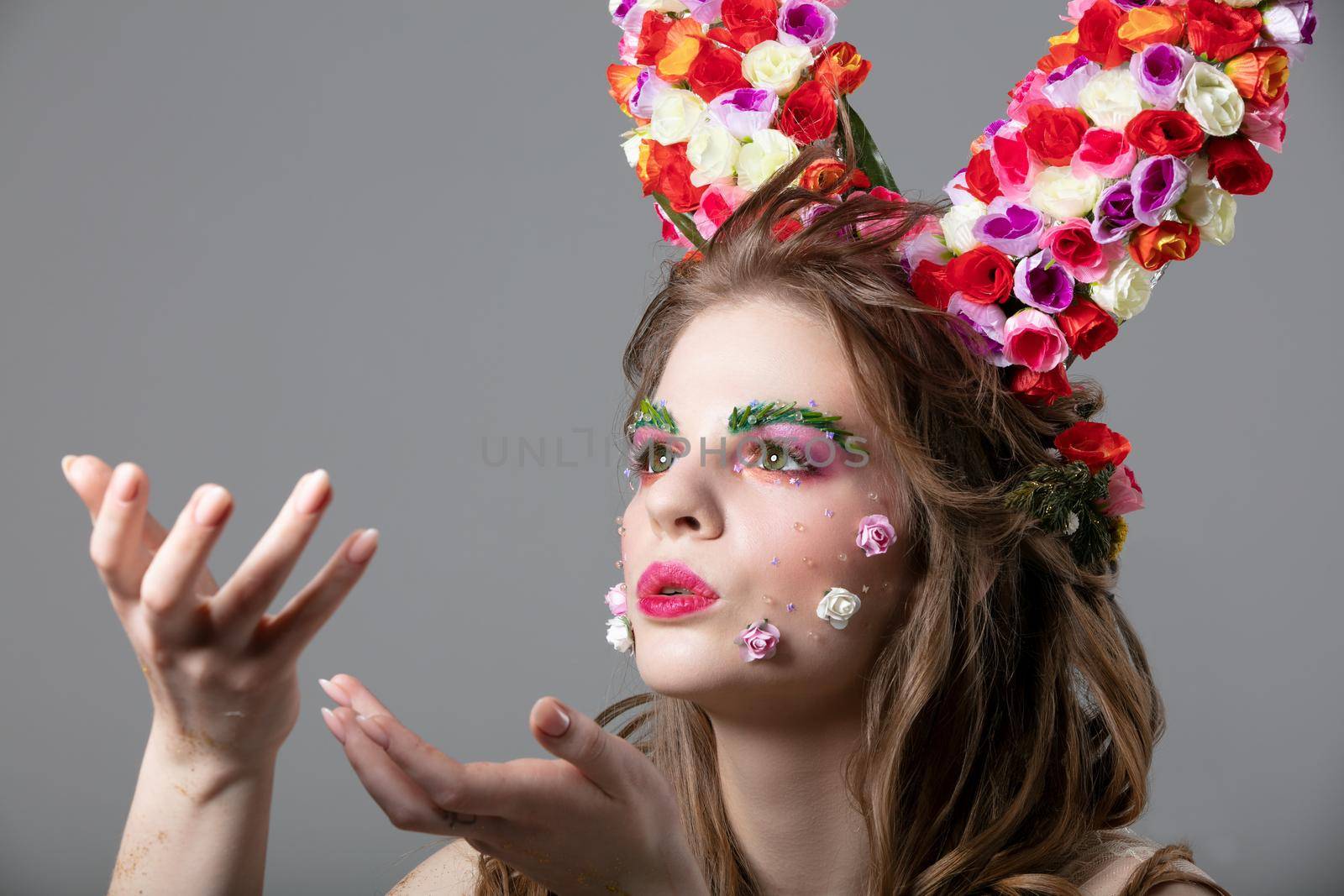 Beautiful flower girl with horns. Goddess Flora. Beautiful woman with fantastic makeup is blowing. Spring girl model.
