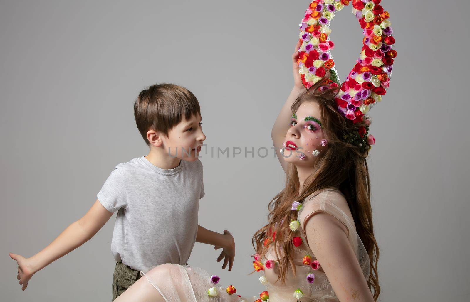An ordinary boy looks at a luxurious girl model. Child with a beautiful girl with flower horns.