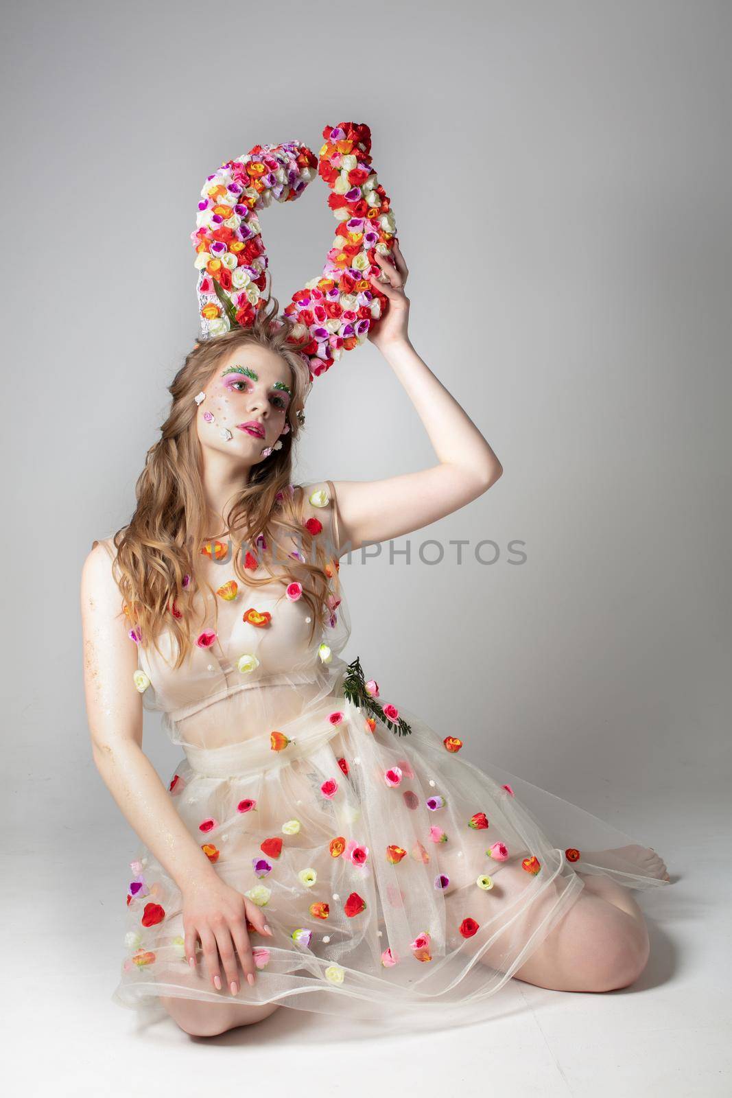 Fantastic girl model with floral horns on a studio background. Maleficent. Spring or summer beauty. Woman in the image of a flower.