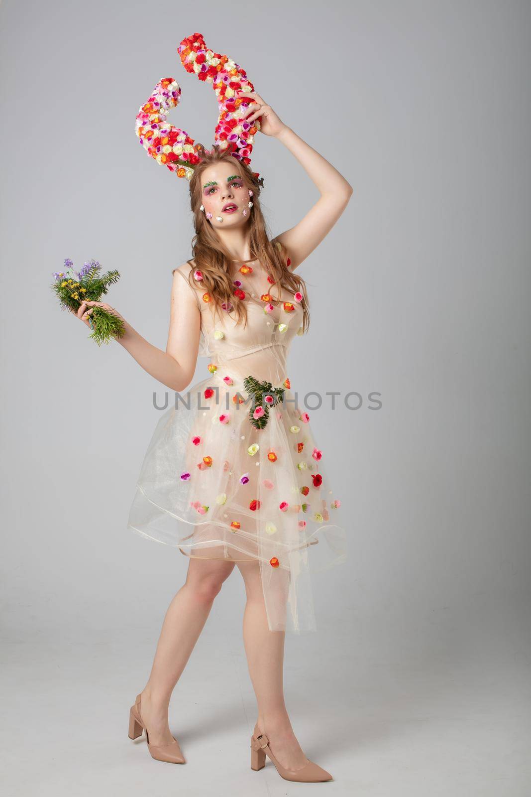Fairy-tale girl model with floral horns bunch on a studio background. Maleficent. Spring or summer beauty. Woman in the image of a flower. Forest woman.