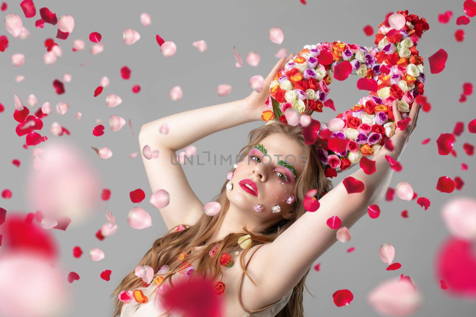 Portrait of a beautiful girl with flower horns in rose petals. Goddess Flora. Beautiful woman with fantastic makeup with flying flowers. Spring girl model.