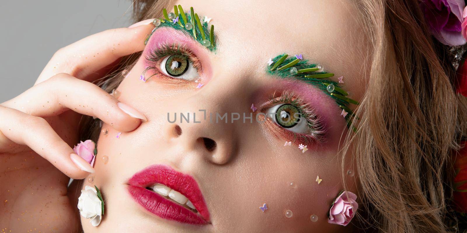 Portrait of a beautiful girl with creative make-up. Summer girl. The face of a luxurious model in flowers. The concept of eyebrow and eyelash extensions.