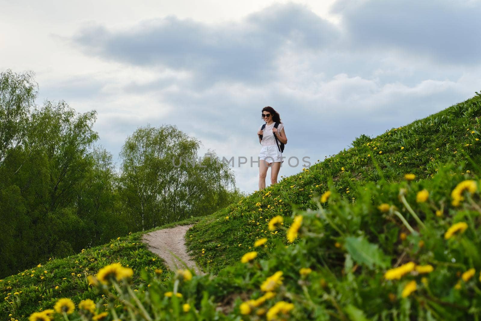 Woman walks along a path among flowers on a summer day.