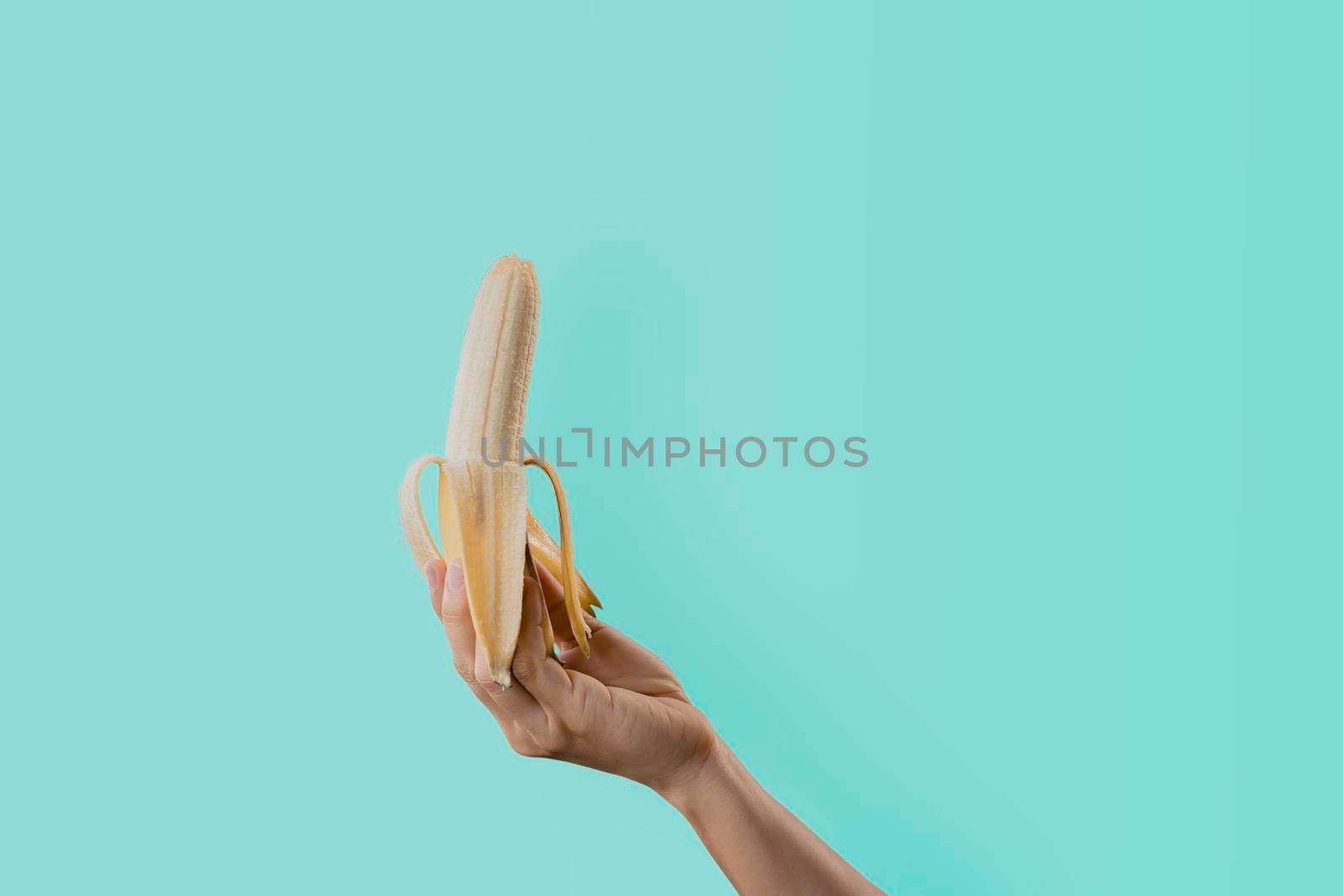 Closeup a woman's hand holding a ripe banana isolated on green pastel colors background