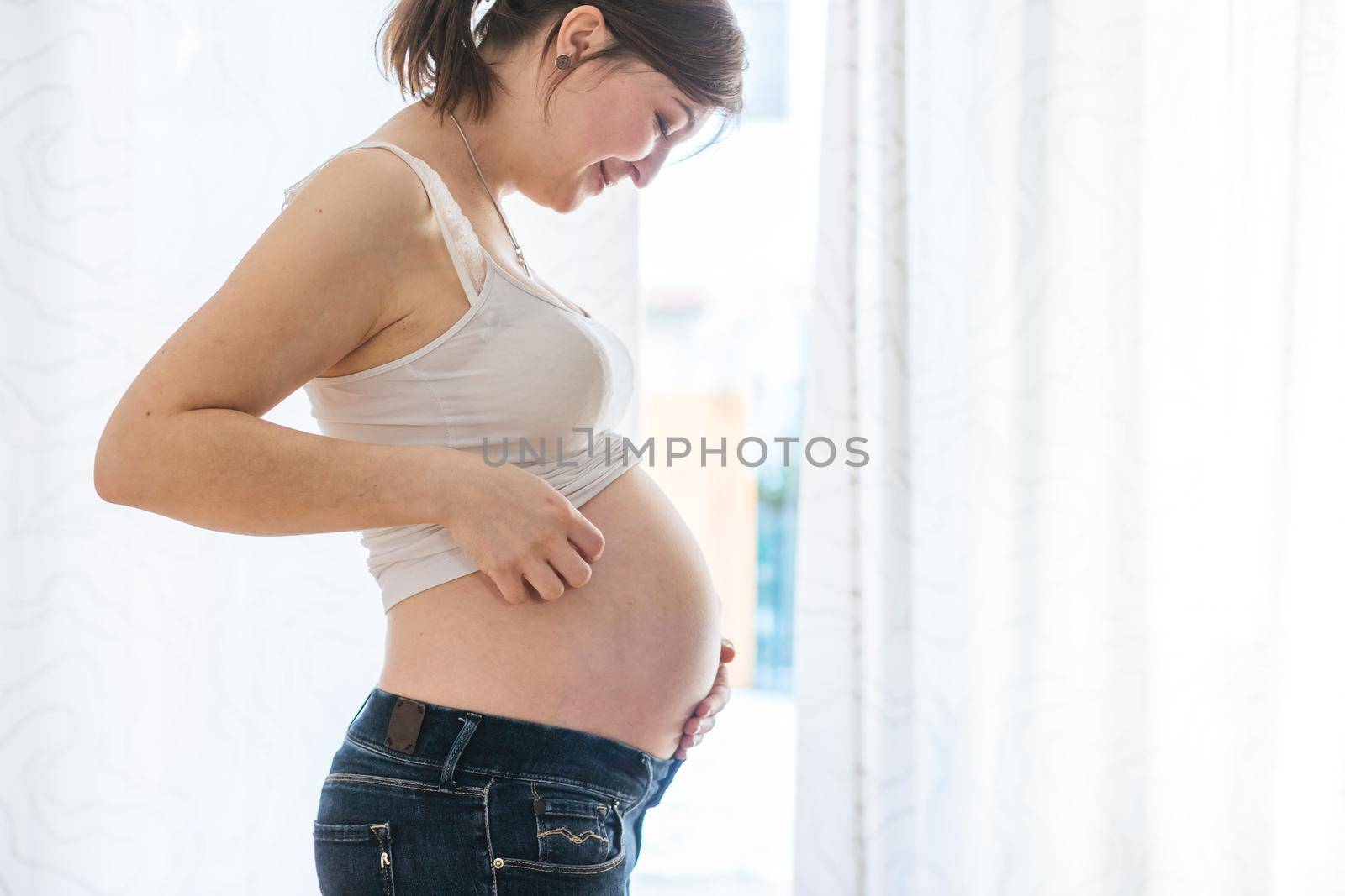 Happy Caucasian pregnant mother touching her tummy, blue jeans, close up