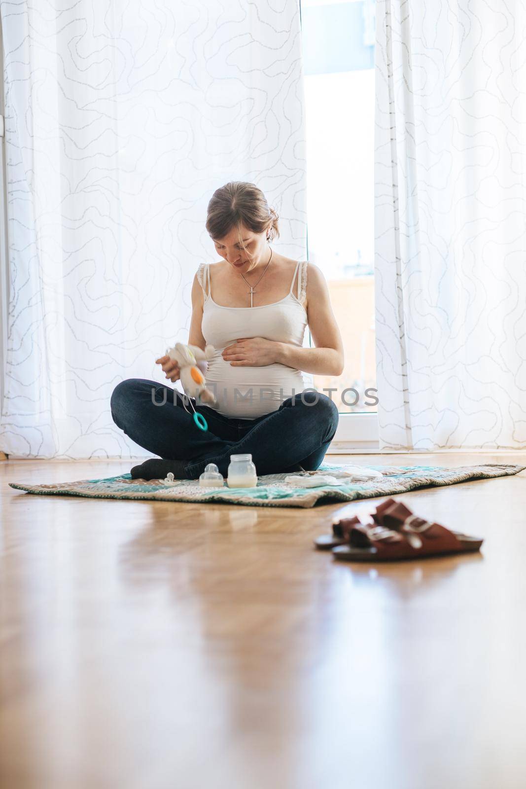 Happy Caucasian pregnant mother is sitting on the floor, touching her tummy, blue jeans