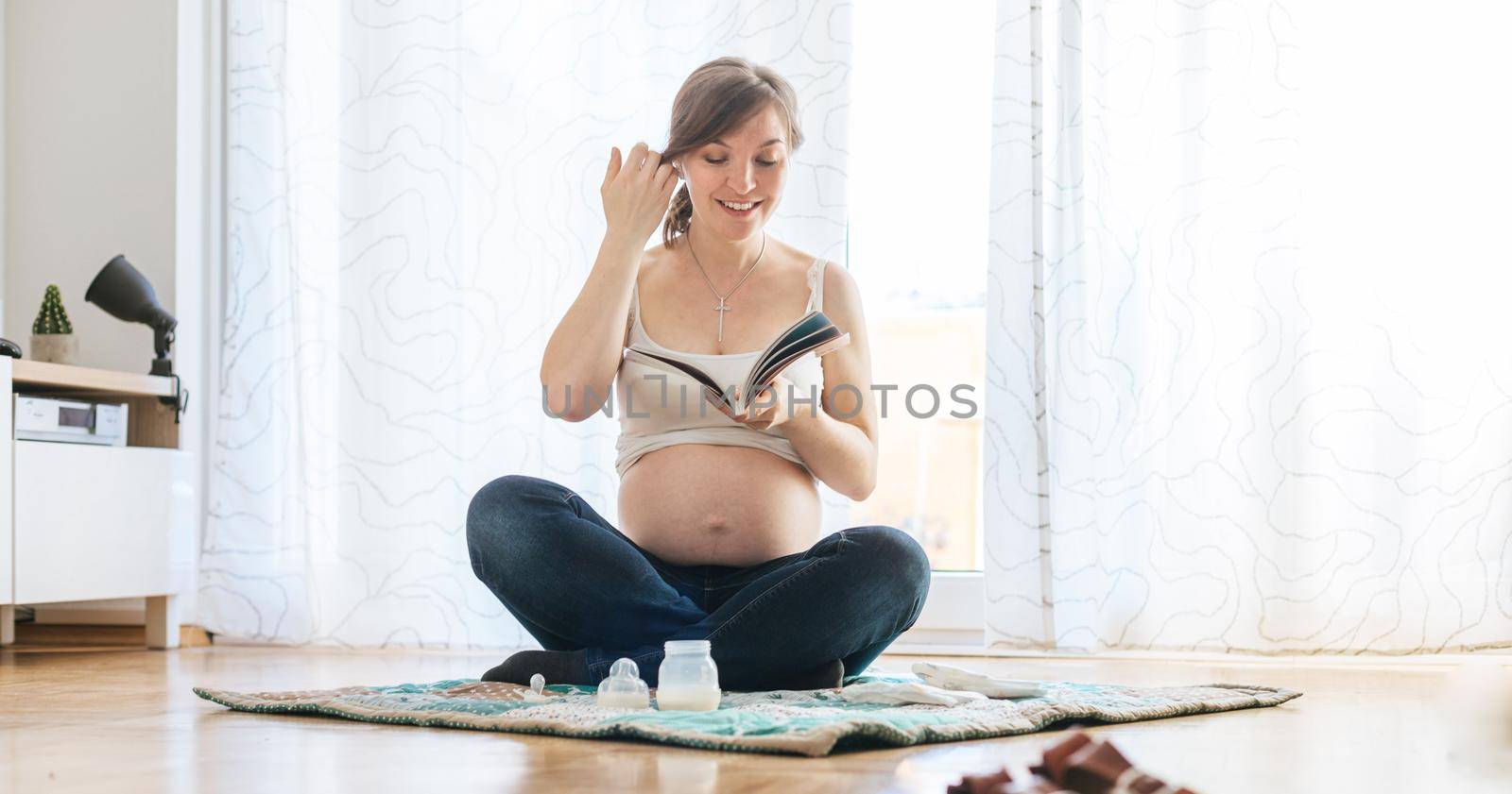 Reading about pregnancy: Happy pregnant mother is sitting on the floor, reading a book by Daxenbichler