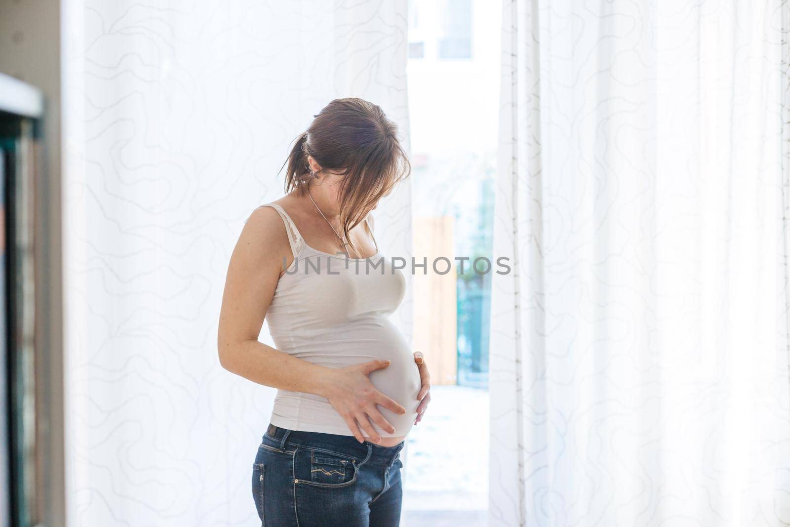 Happy Caucasian pregnant mother touching her tummy, blue jeans, close up