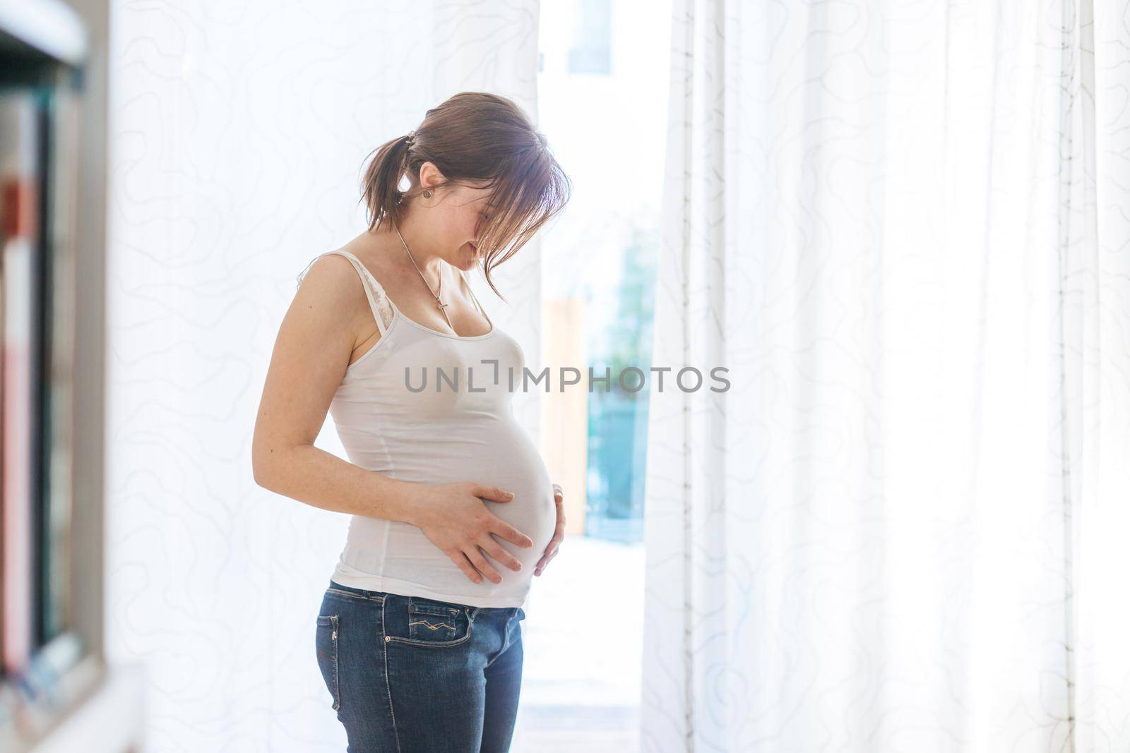 Happy Caucasian pregnant mother touching her tummy, blue jeans, close up