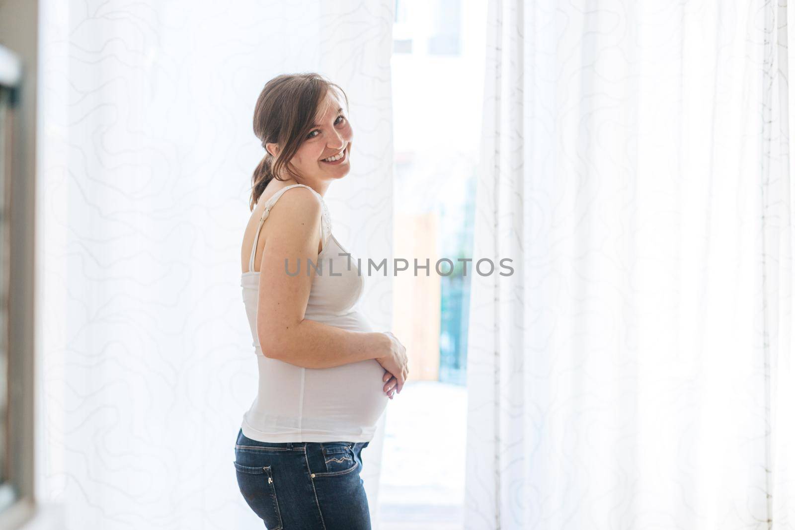 Happy Caucasian pregnant mother touching her tummy, blue jeans, close up