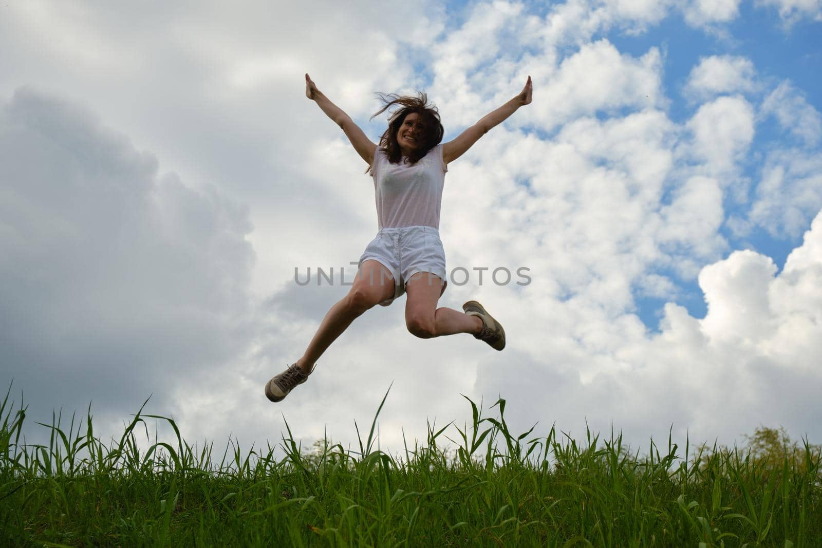 Happy girl jumping against the background of blue sky and clouds by vollirikan