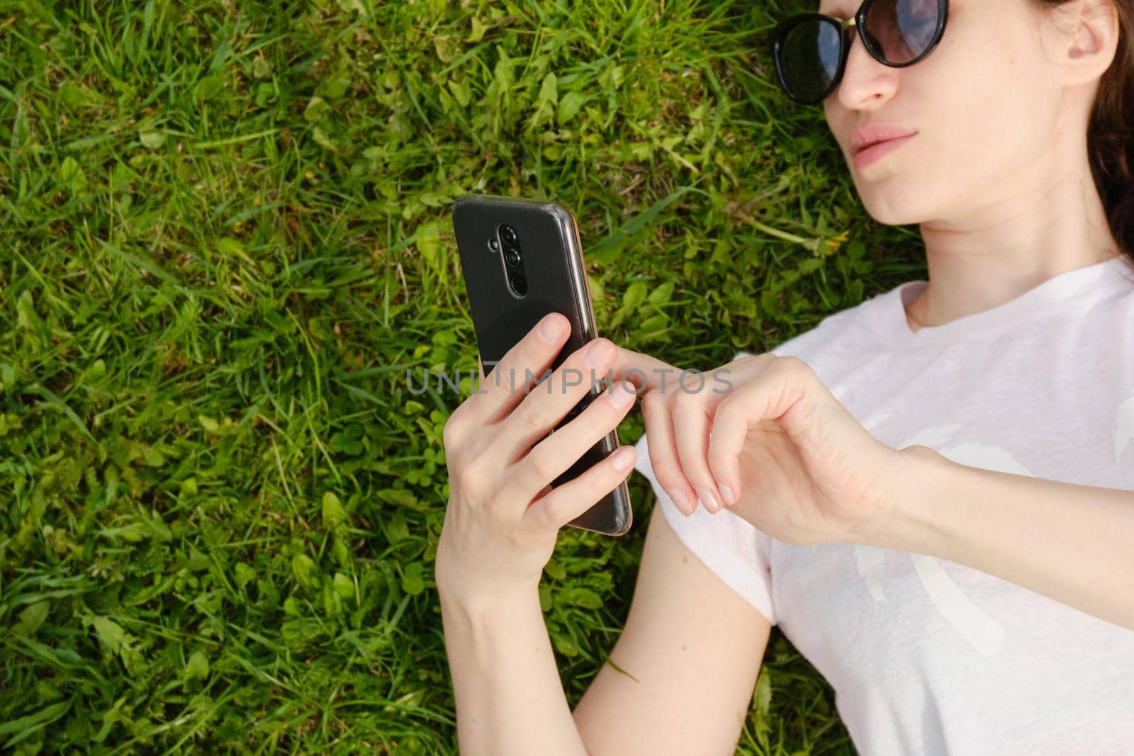 Girl with glasses lies on green grass and holds a smartphone by vollirikan