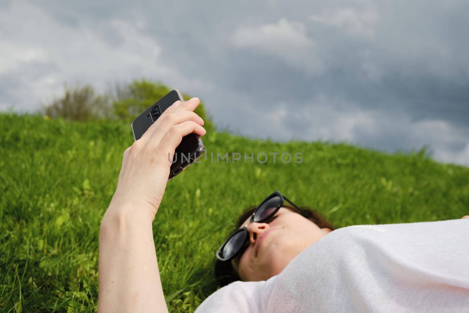 Girl with glasses lies on green grass and holds a smartphone by vollirikan