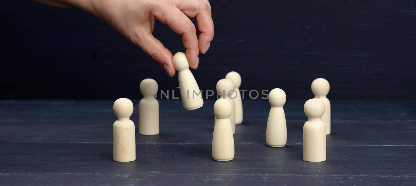 female hand holds a wooden figurine above the crowd. The concept of finding employees, talented and unique employees. Career growth, choice of a leader, banner