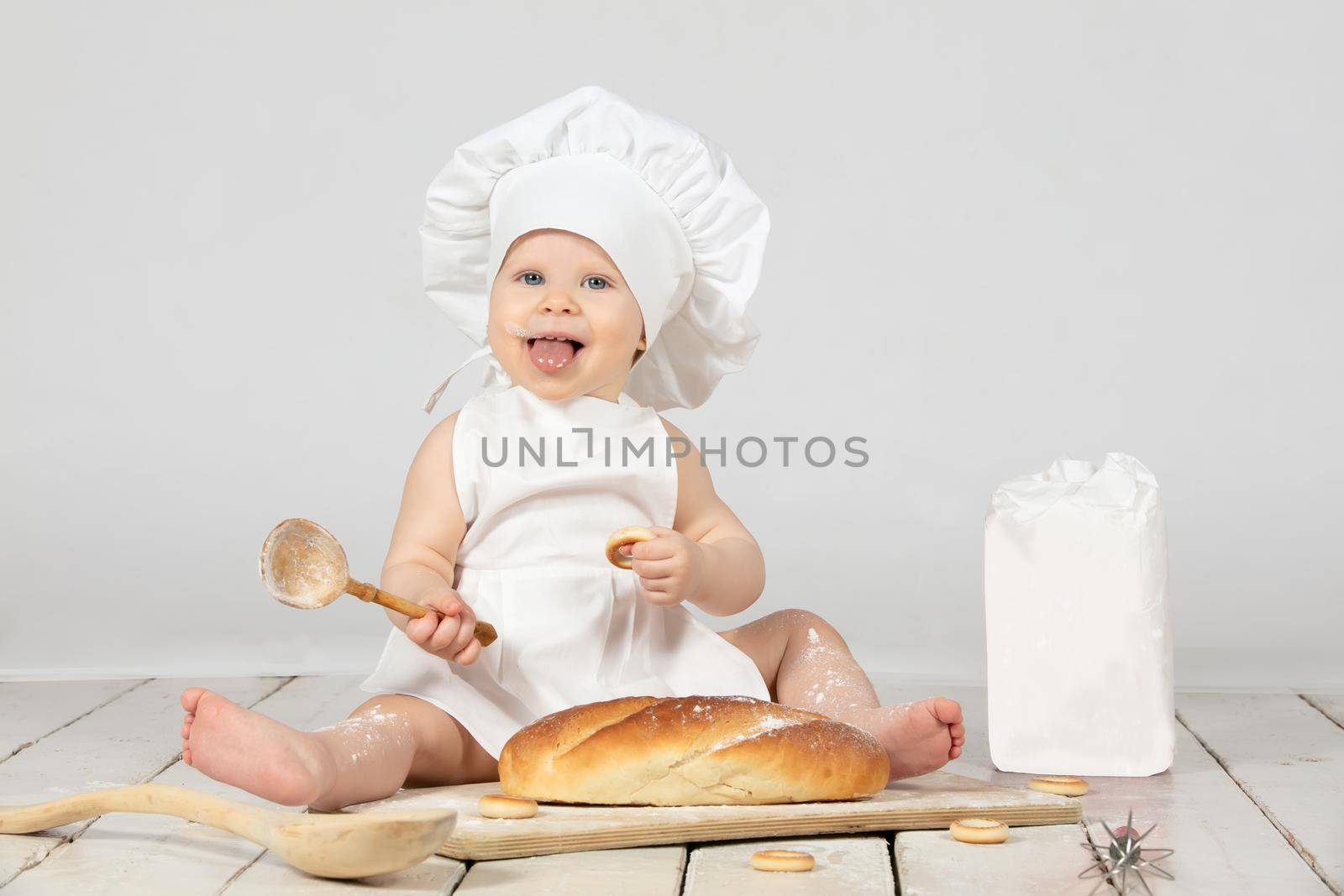 Child cook. Beautiful little girl in cook clothes with long loaf and flour. The child is one year old. Funny baby is laughing. Little chef. The concept of baking bakery products.
