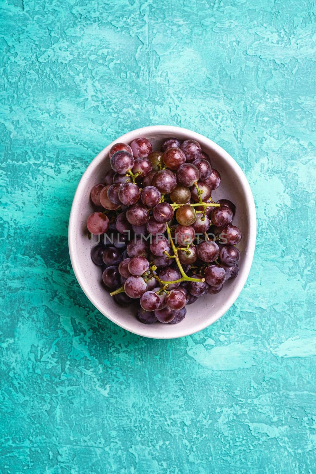 Fresh ripe grape berries in bowl on turquoise textured background, top view by Frostroomhead