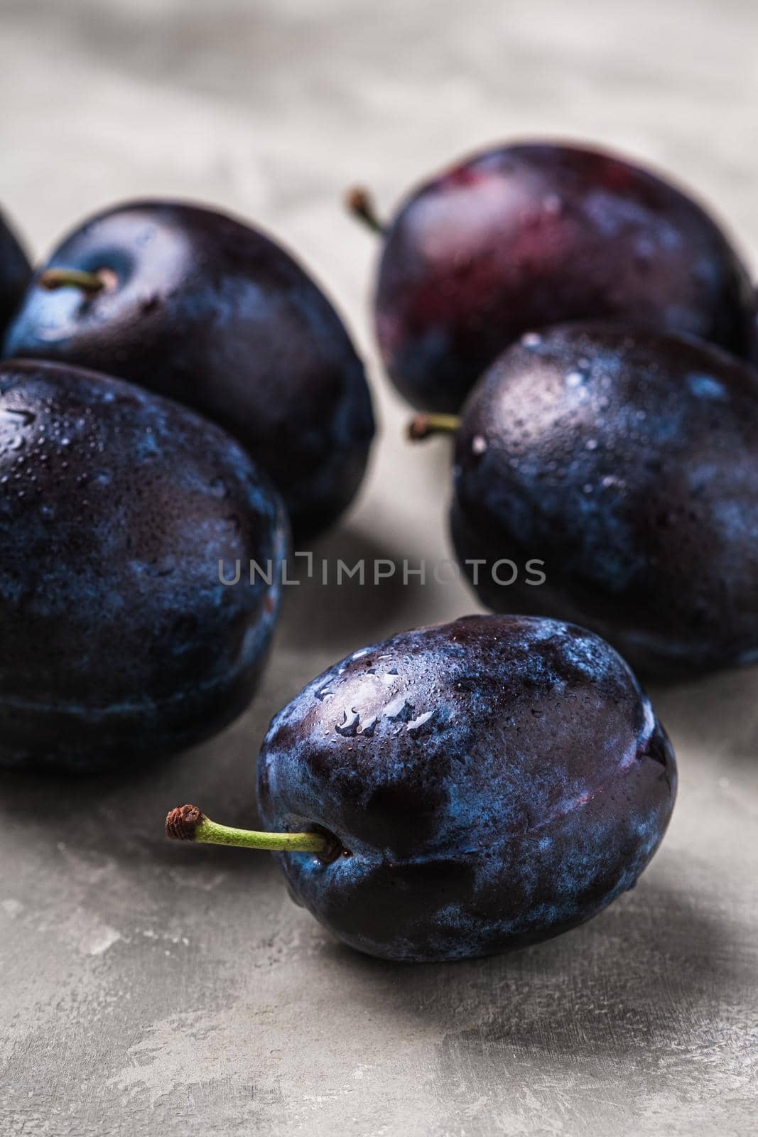 Fresh ripe plum fruits with water drops on stone concrete background, angle view macro by Frostroomhead
