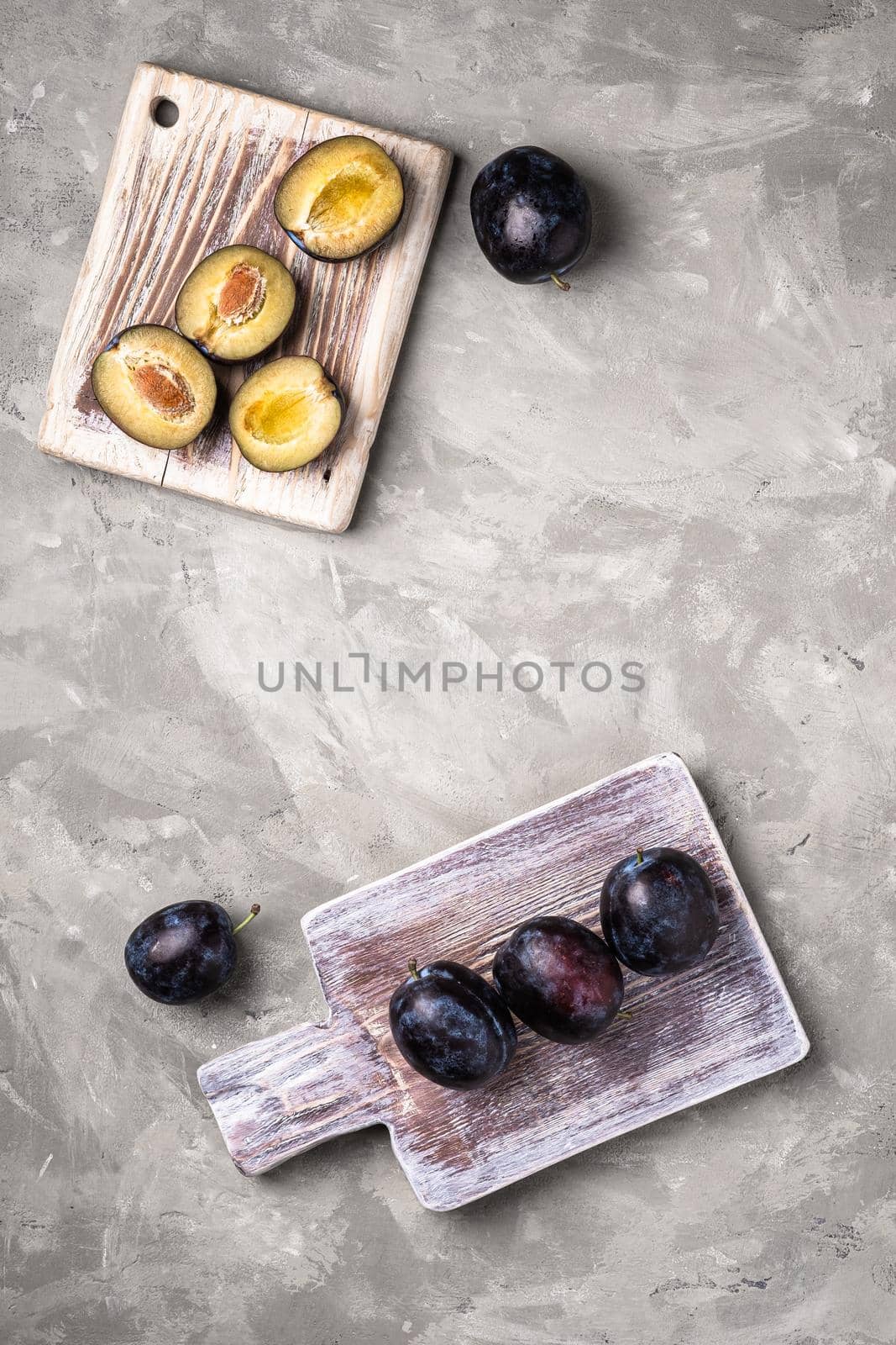 Fresh ripe plum fruits whole and sliced on wooden cutting boards, stone concrete background, top view copy space