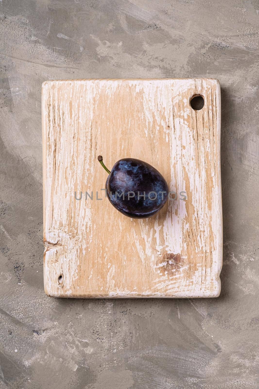 Fresh ripe plum fruit on wooden cutting board, stone concrete background, top view