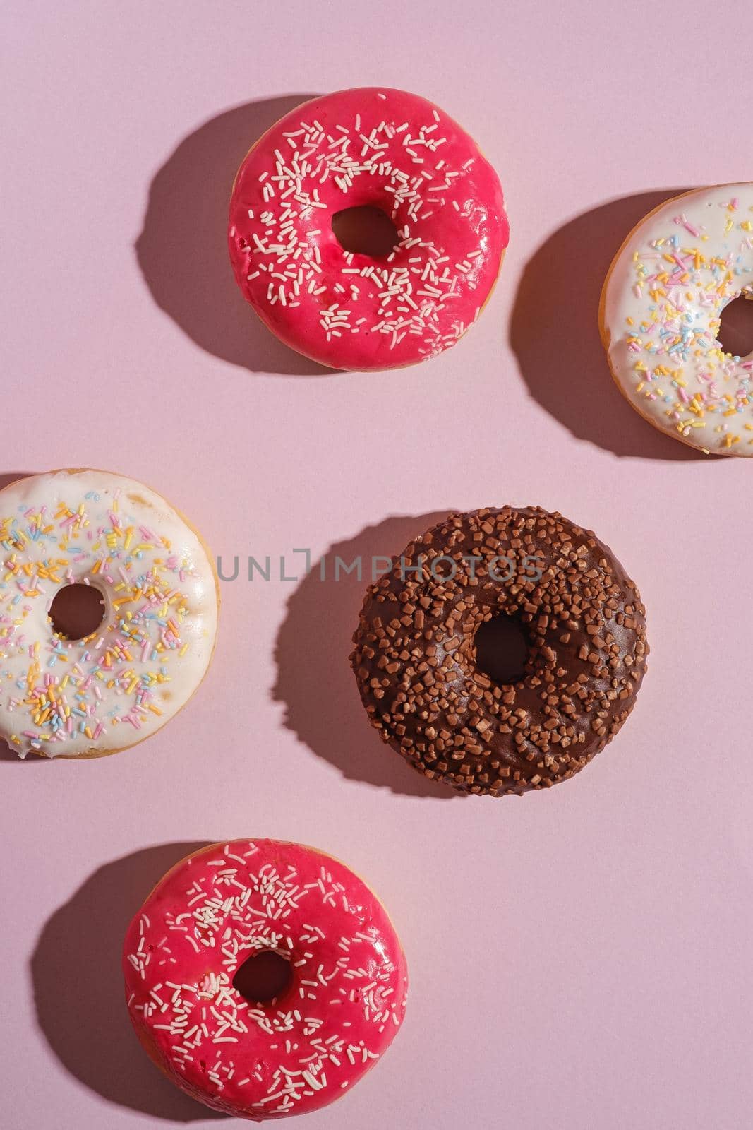 Chocolate, pink and vanilla donuts with sprinkles, sweet glazed dessert food on pink minimal background, top view
