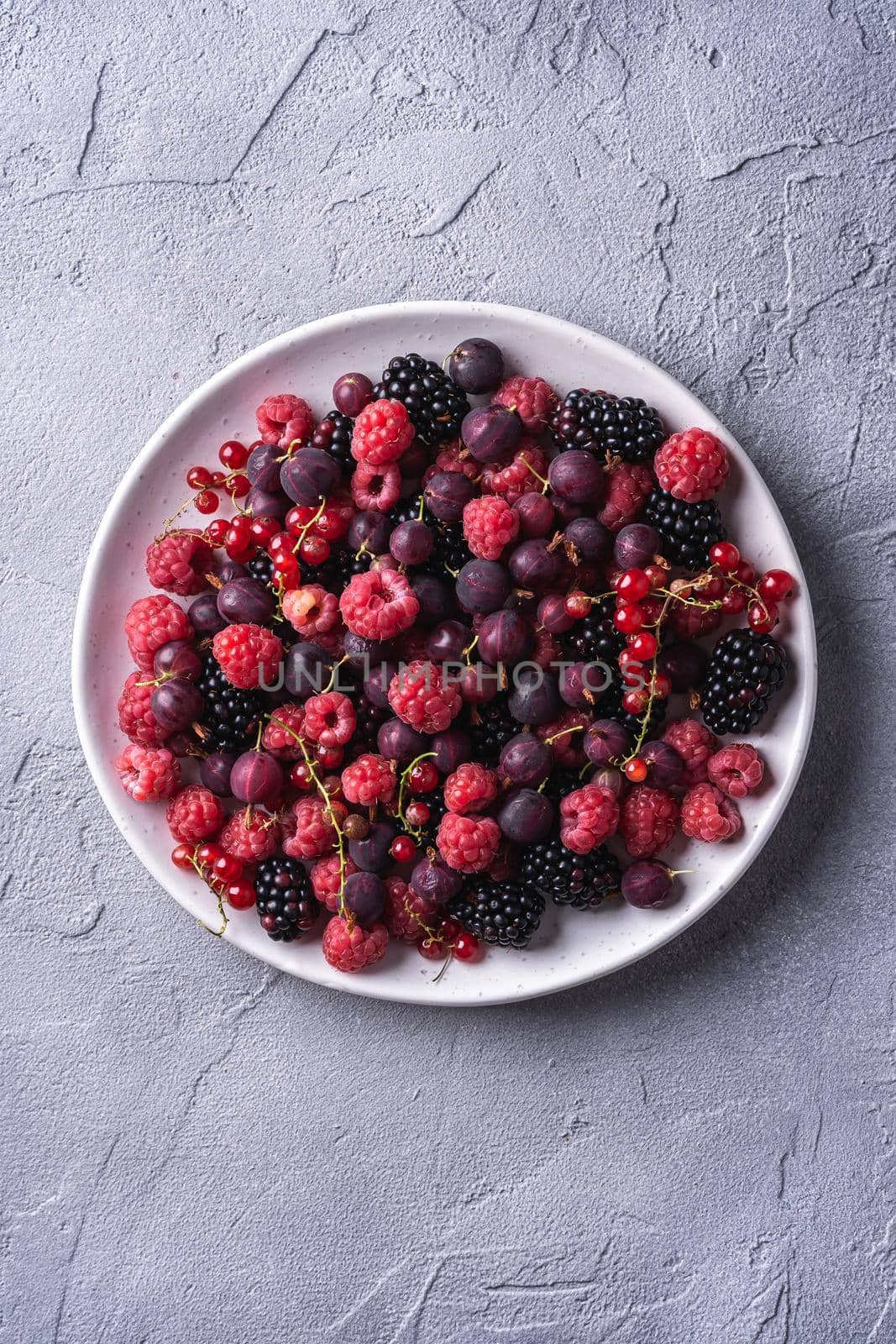 Tasty fresh ripe raspberry, blackberry, gooseberry and red currant berries in plate, healthy food fruit on stone concrete background, top view by Frostroomhead