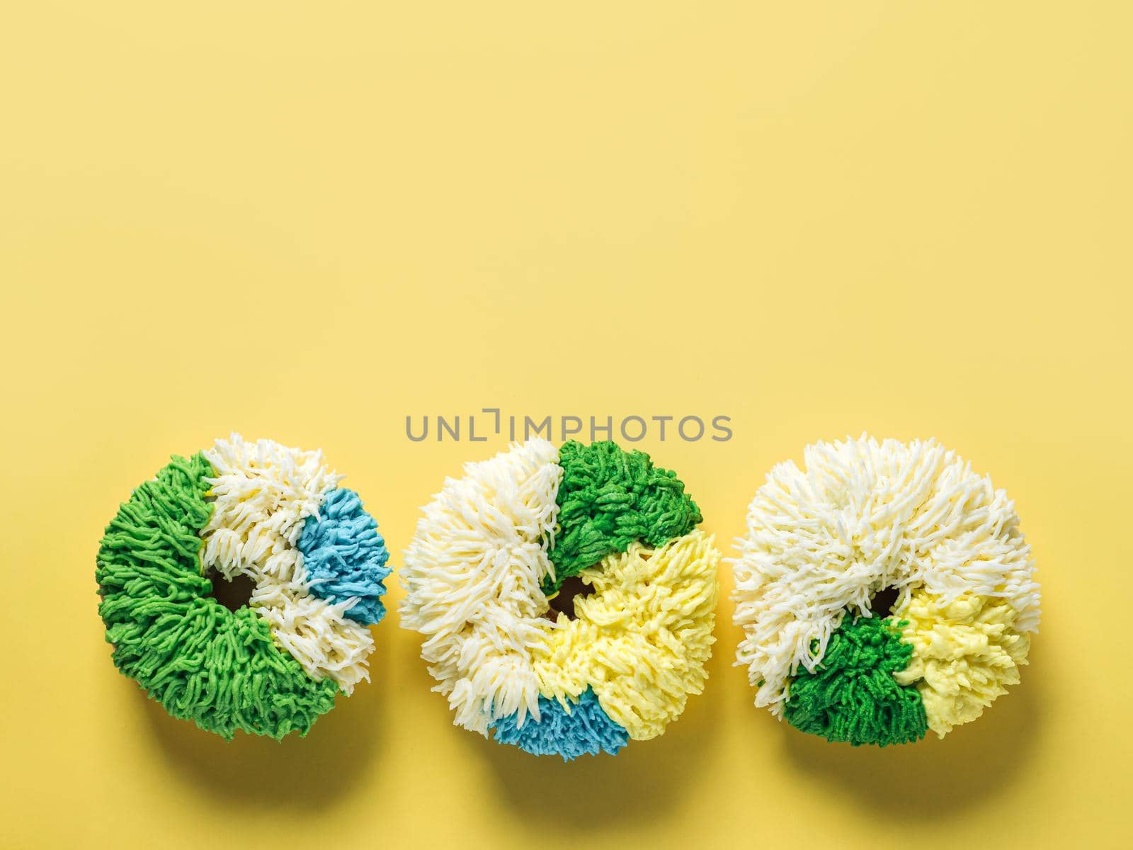 Shag donuts on bright yellow background. Unusual trendy colorful donuts with vanilla buttercream. Copy space. Top view or flat lay.