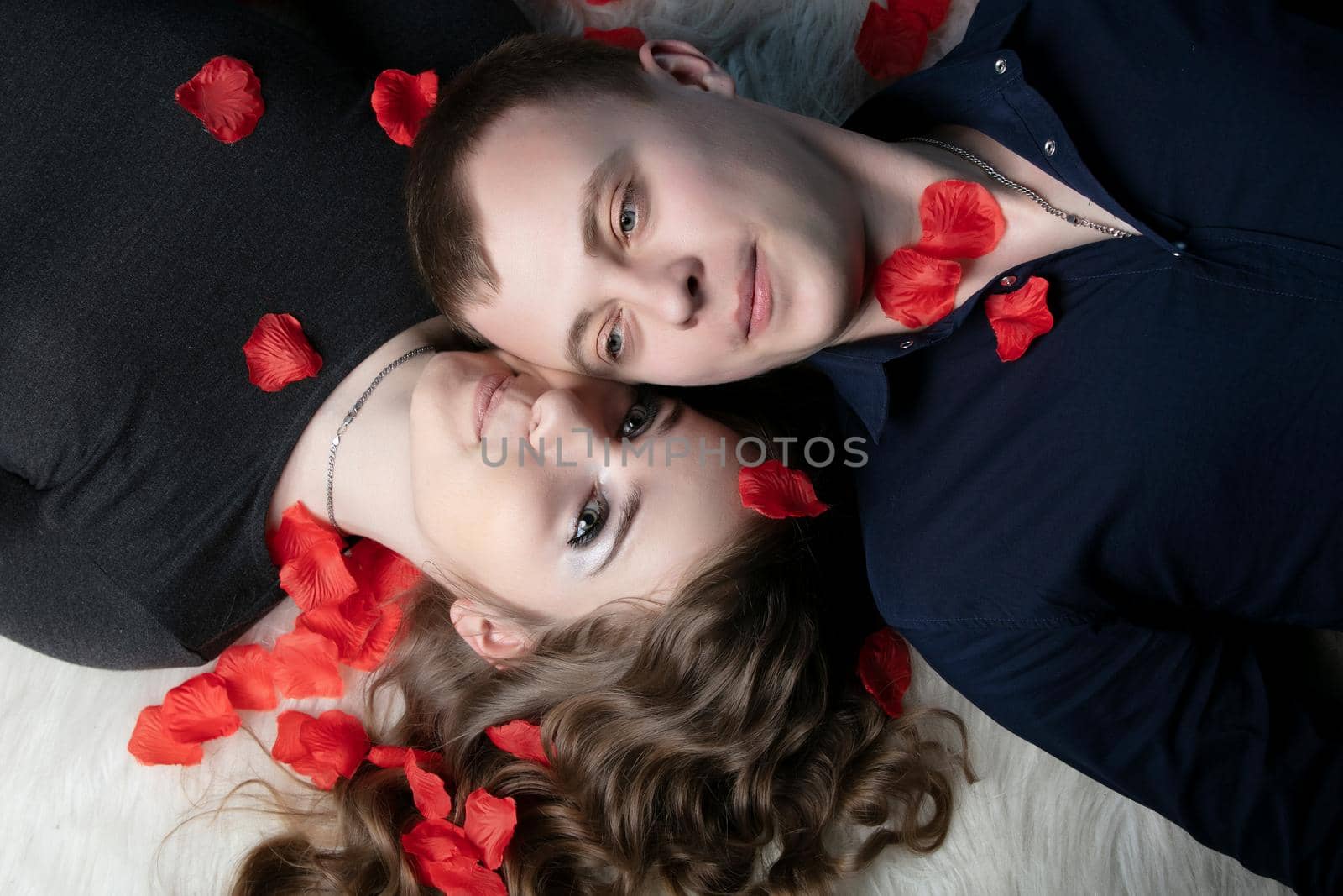 Loving couple. Man and woman lie in rose petals. Beautiful young husband and wife. by Sviatlana
