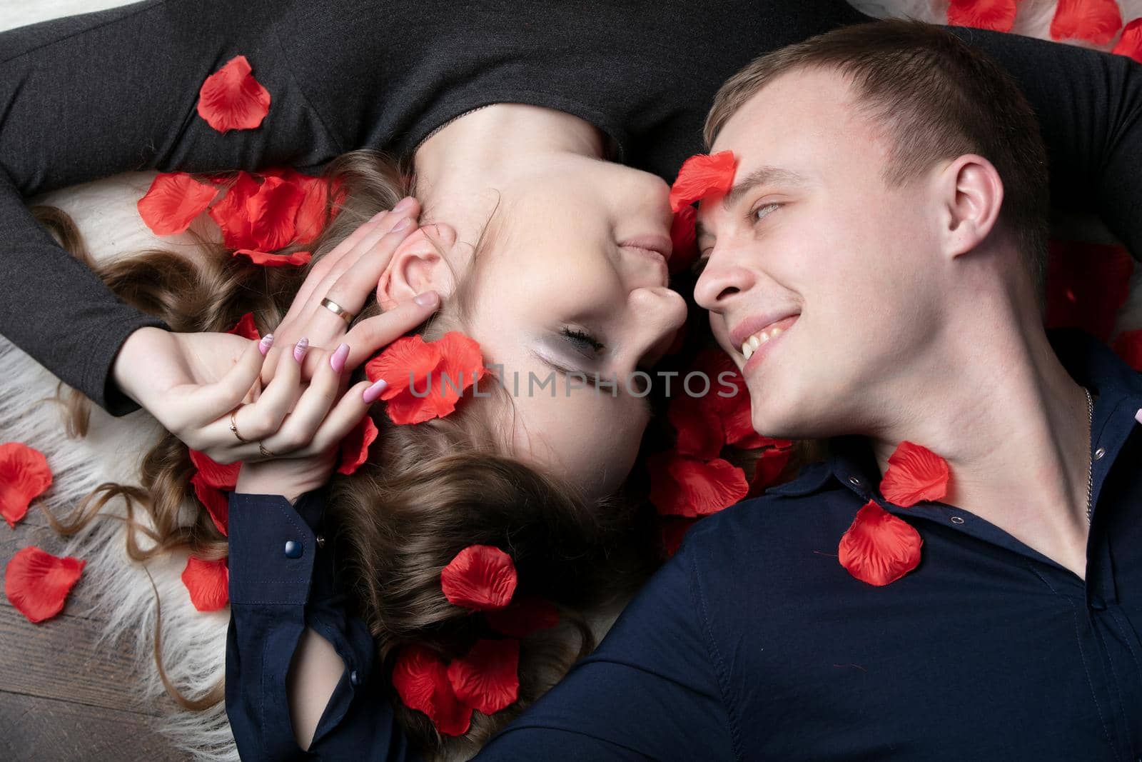 Loving couple. Man and woman in rose petals. Beautiful young husband and wife.Close-up man and woman together.Valentine's day. by Sviatlana