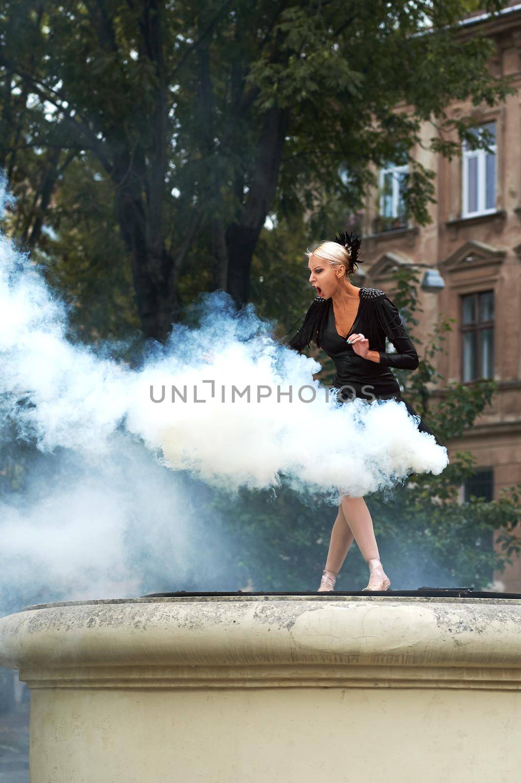 Vertical shot of a beautiful ballerina in black outfit dancing in the smoke on the city street expressive fierce vogue artistic.
