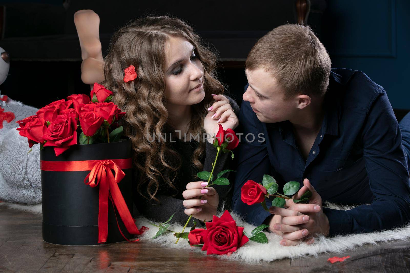 Beautiful young couple at home. Hugs, kisses and enjoys spending time together, celebrating Valentine's Day with red roses.
