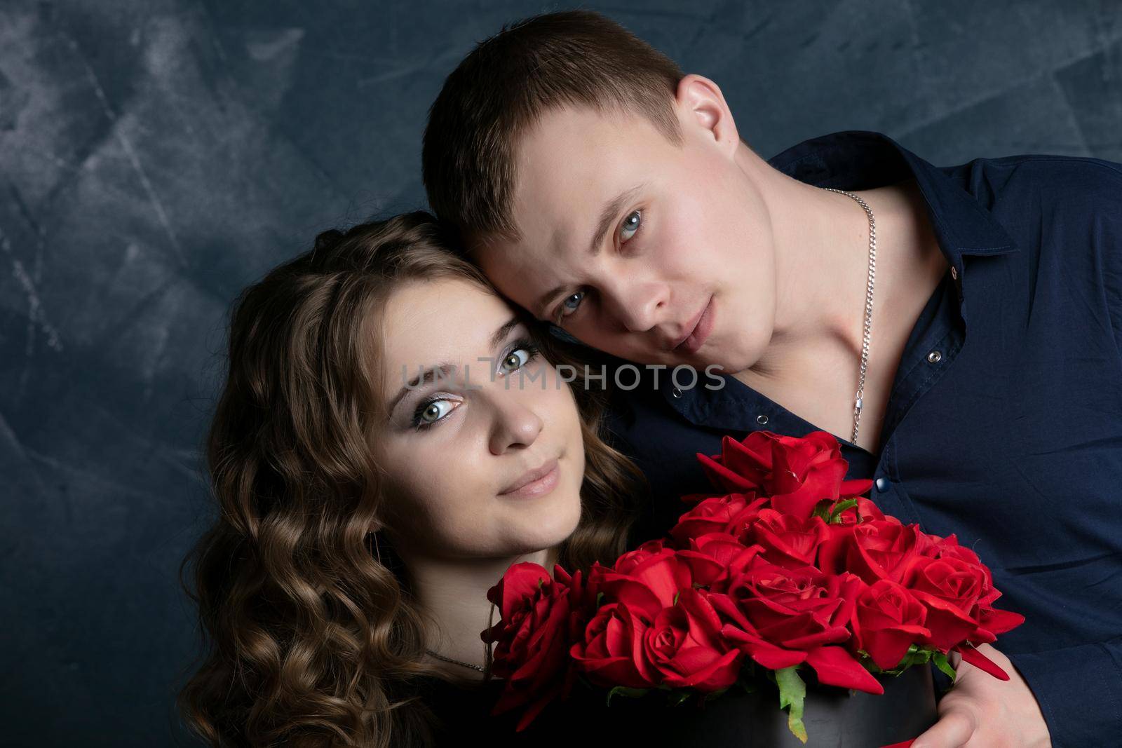 Portrait of a beautiful couple in love on a dark background. Faces of a girl and a guy close-up with roses. Valentine's Day. by Sviatlana