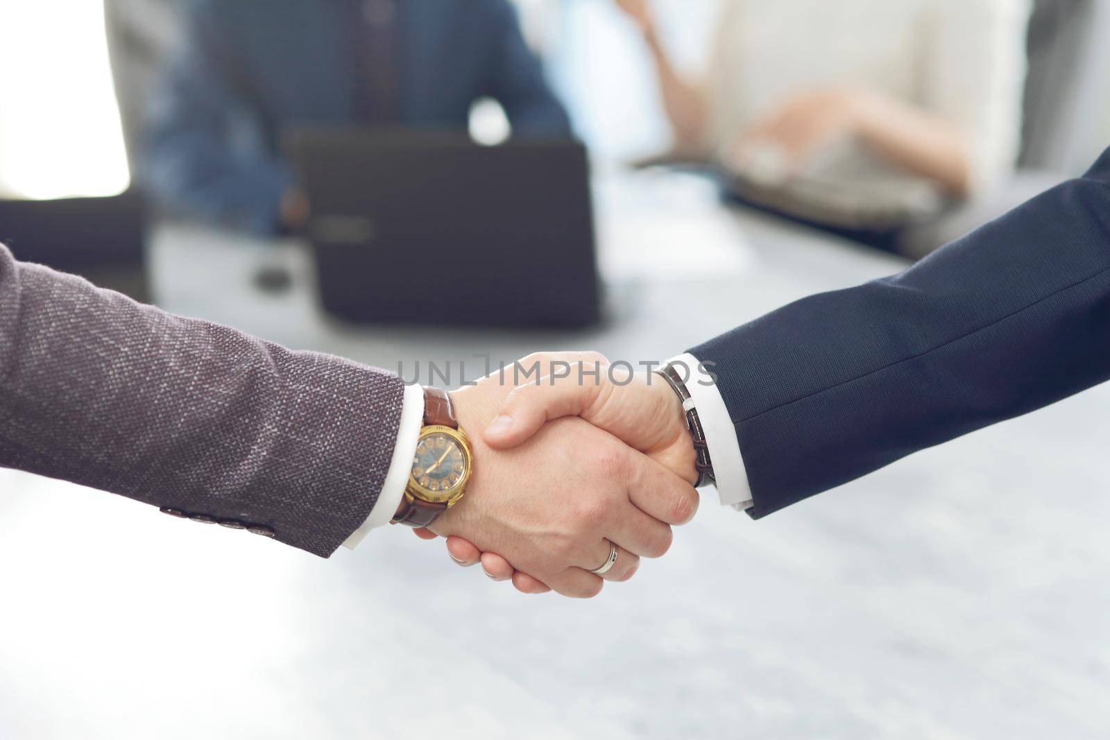 Business people shaking hands finishing a meeting in the background of their work team. 