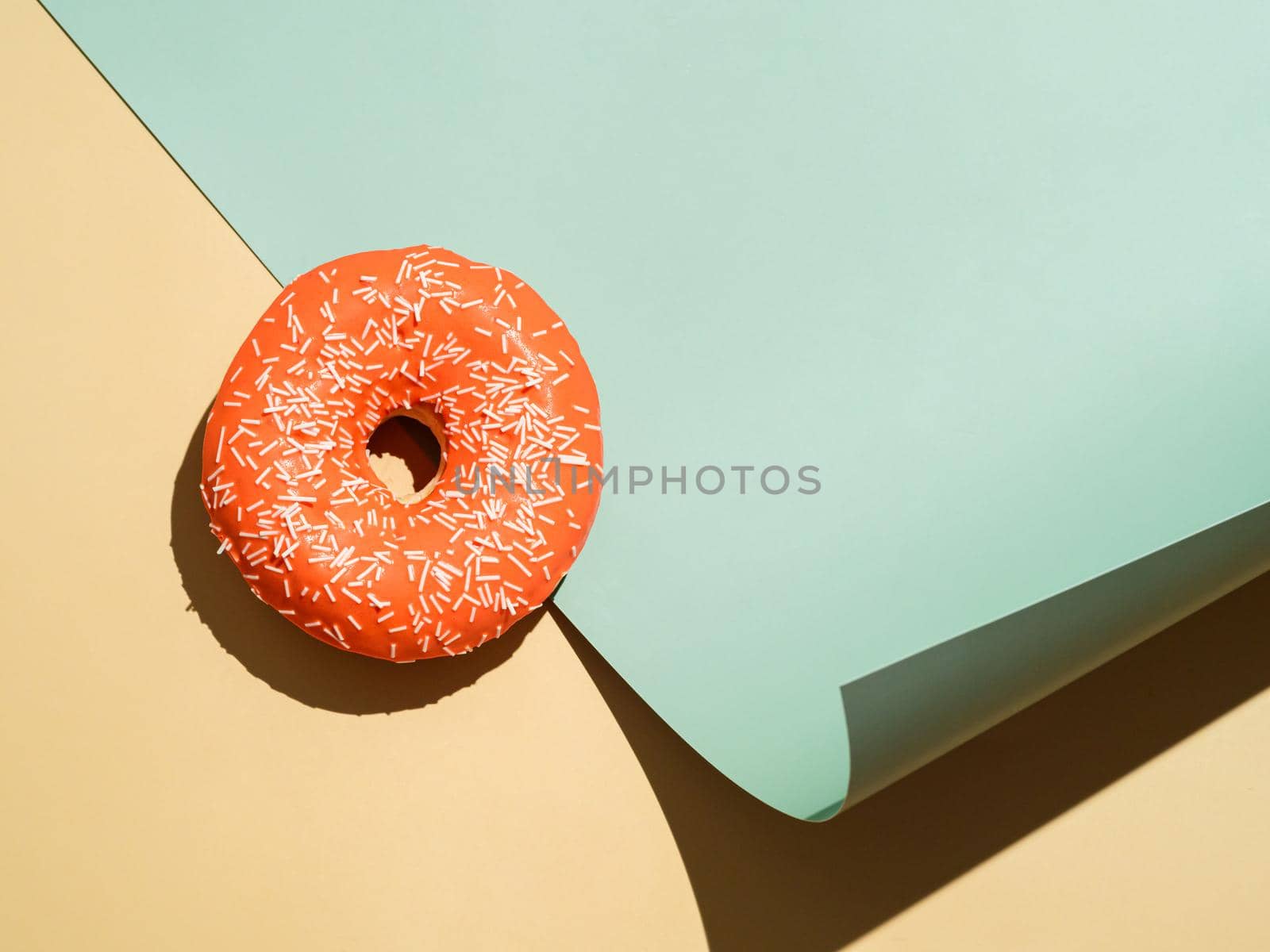 Creative layout made with delicious glazed donut.Flat lay orange glazed donut or doughnut on pastel cream beige and soft green colors neutral background. Bright sun light with hard shadows, copy space