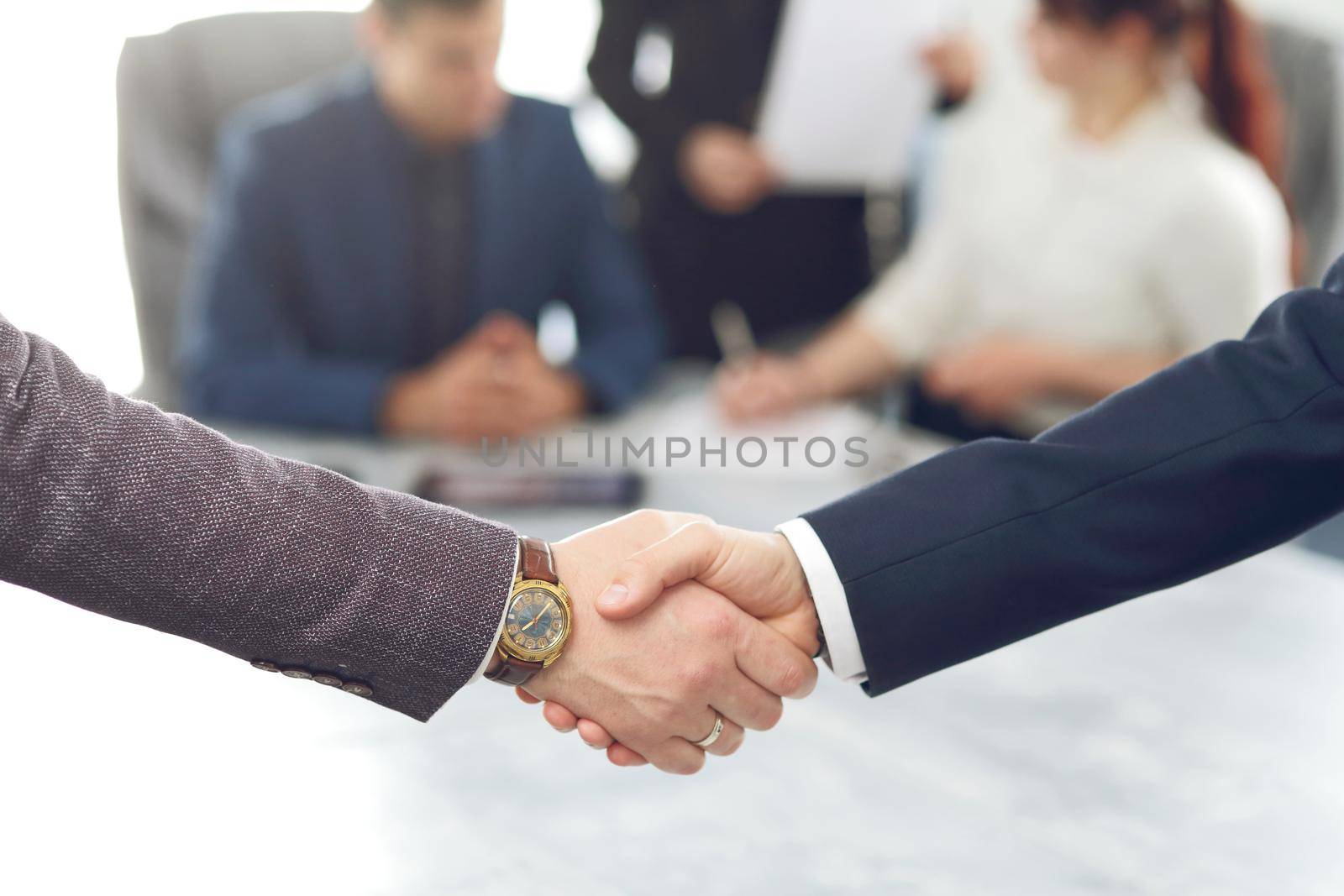 Business people shaking hands finishing a meeting in the background of their work team. 