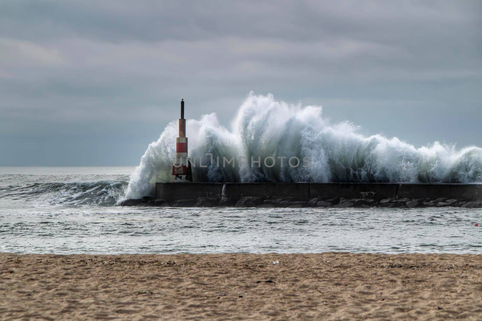 Giant waves breaking on the breakwater and the lighthouse on Aguda Beach, Miramar, Arcozelos town