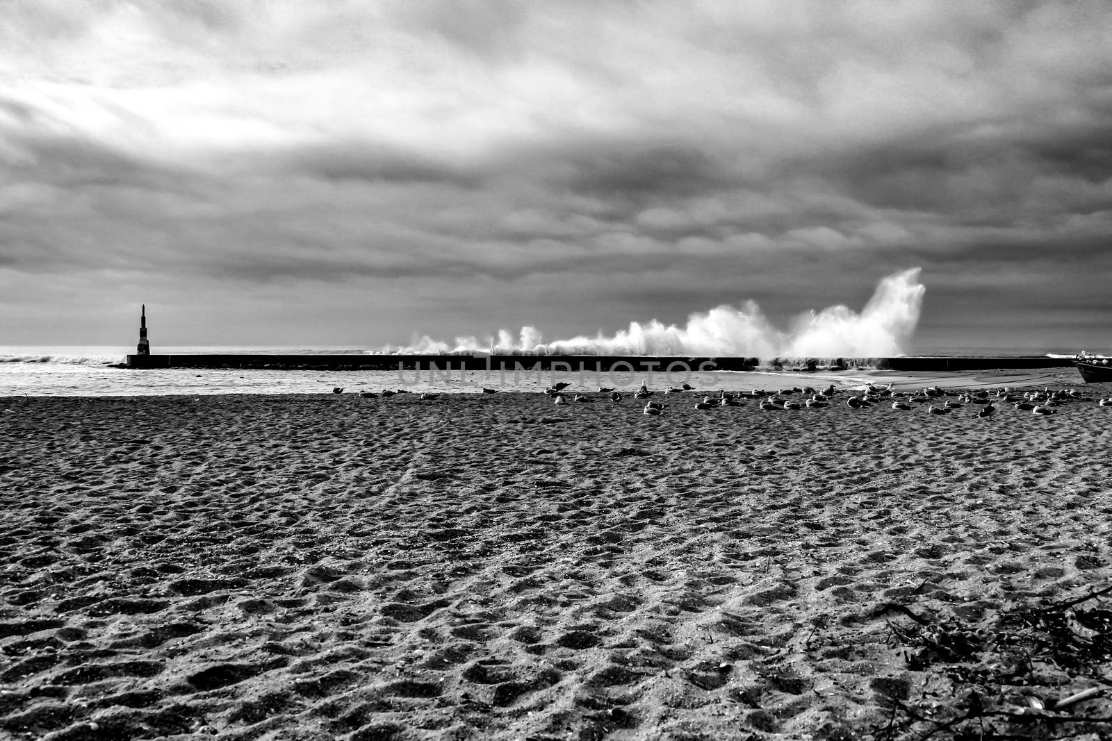 Giant waves breaking on the breakwater and the lighthouse on Aguda Beach, Miramar, Arcozelos town