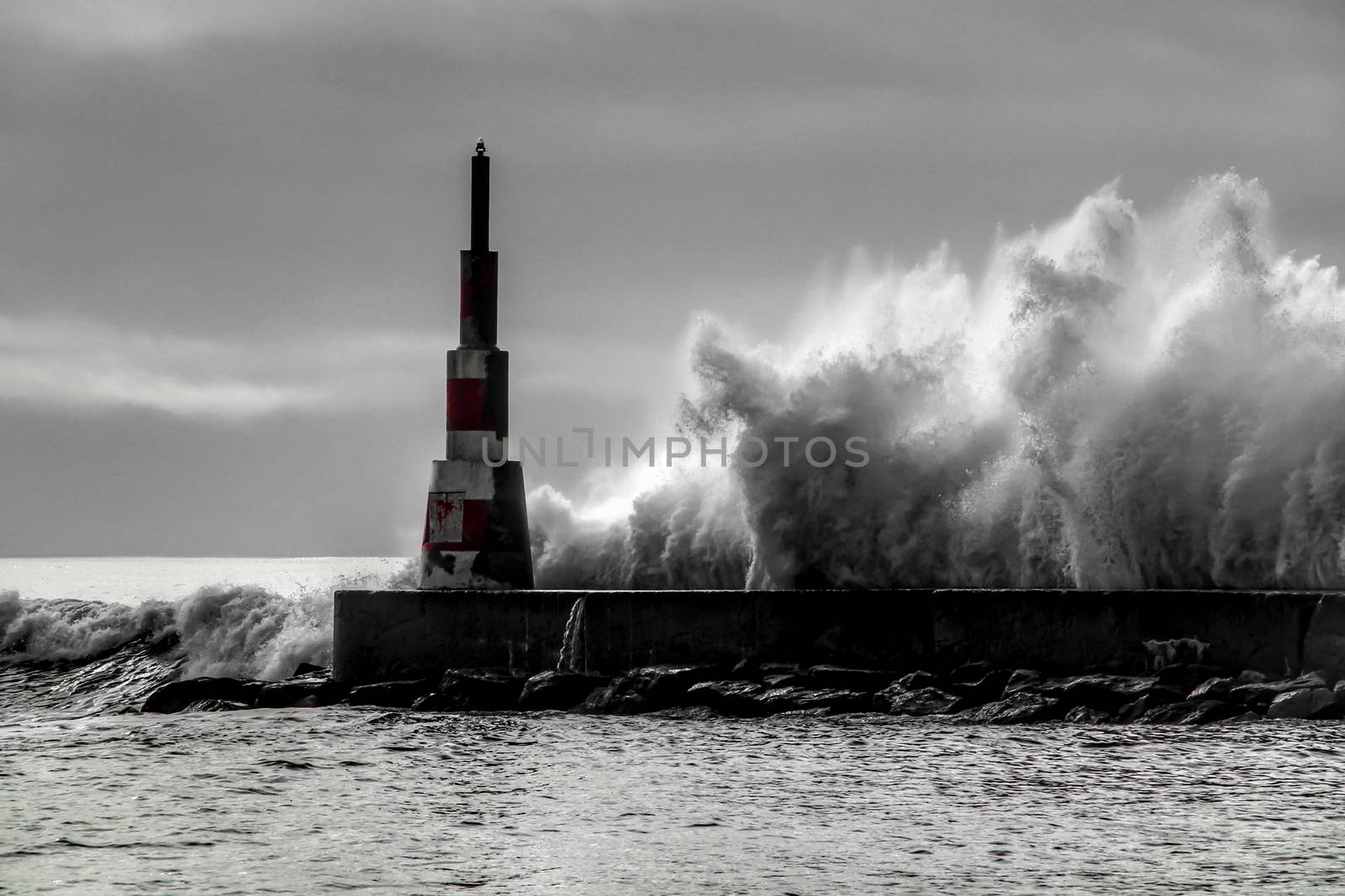 Giant waves breaking on the breakwater and the lighthouse on Aguda Beach, Miramar, Arcozelos town