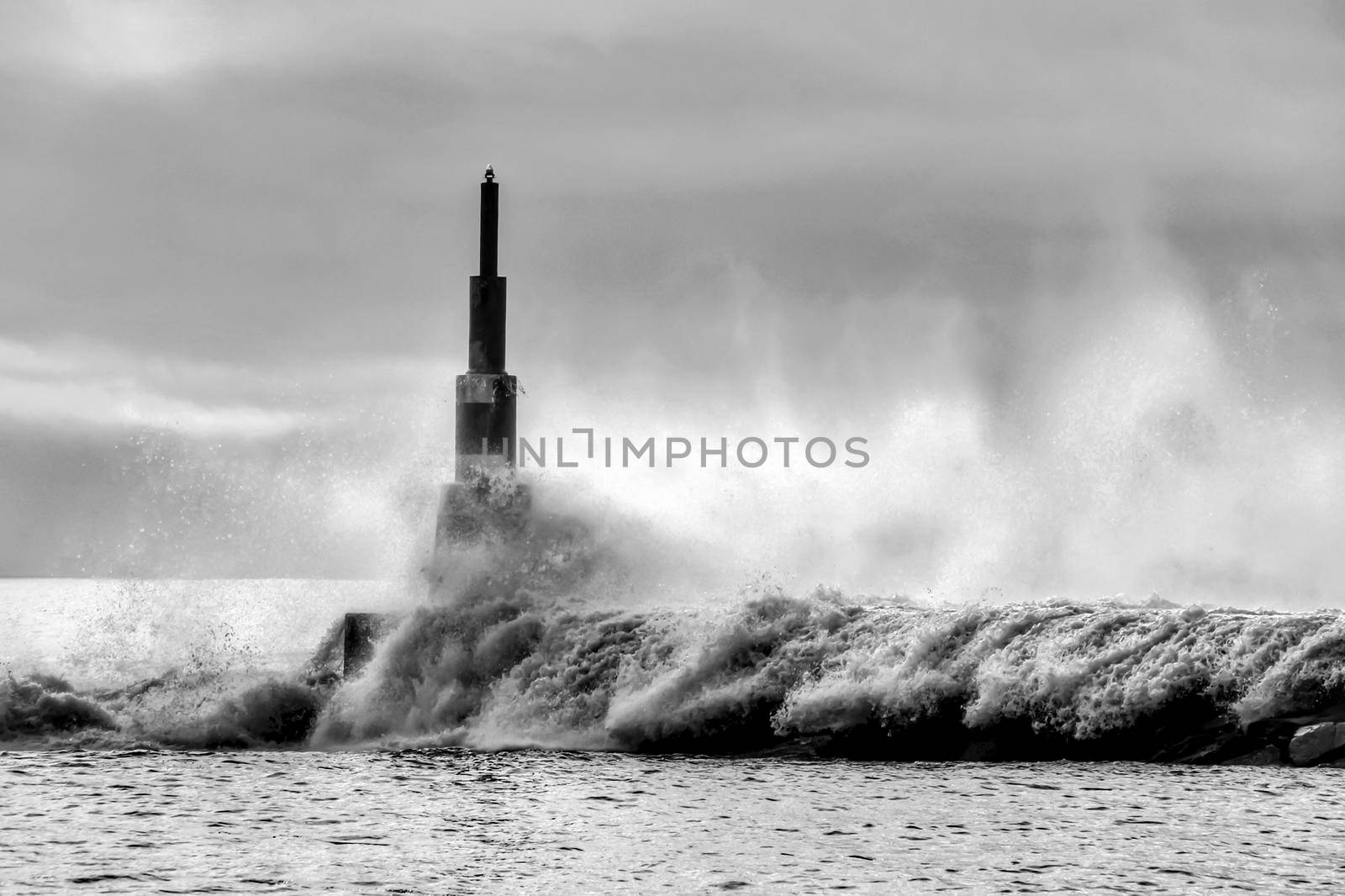 Giant waves breaking on the breakwater and the lighthouse on Aguda Beach, Miramar, Arcozelos town