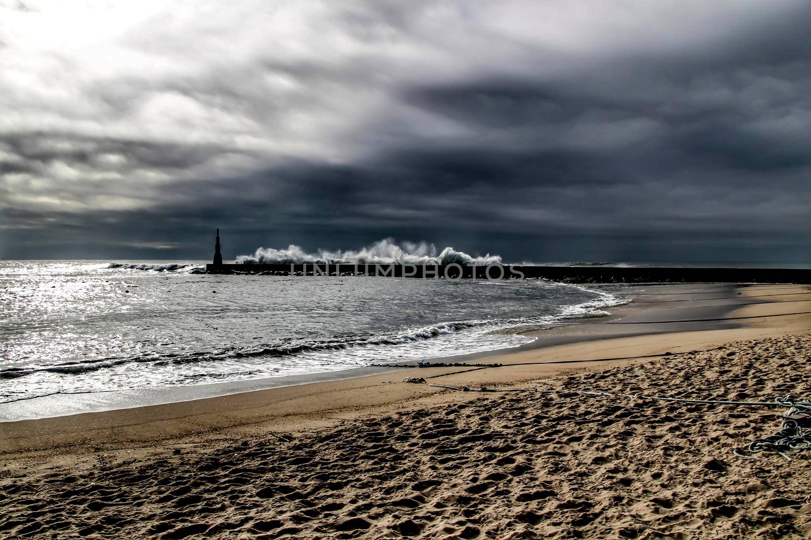 Giant waves breaking on the breakwater and the lighthouse on Aguda Beach, Miramar, Arcozelos town