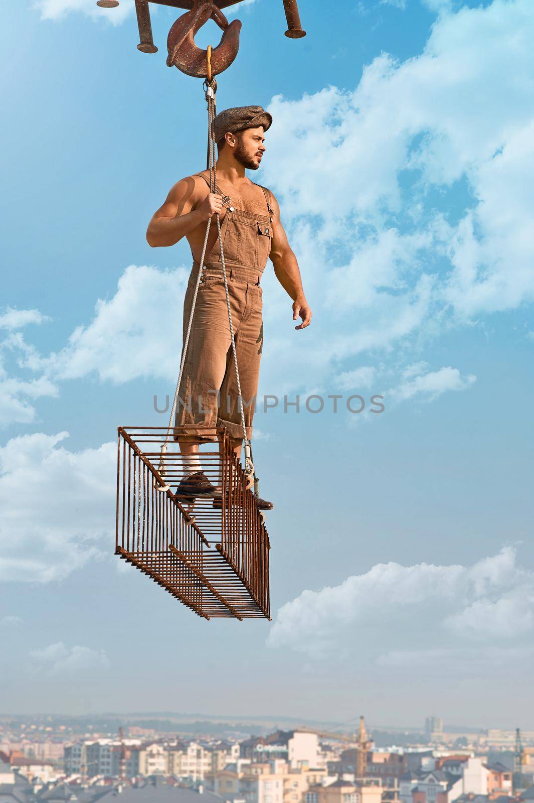 Gonna build this up. Vertical shot of a muscular old fashioned construction worker posing on a metal crossbar blue skies on the background