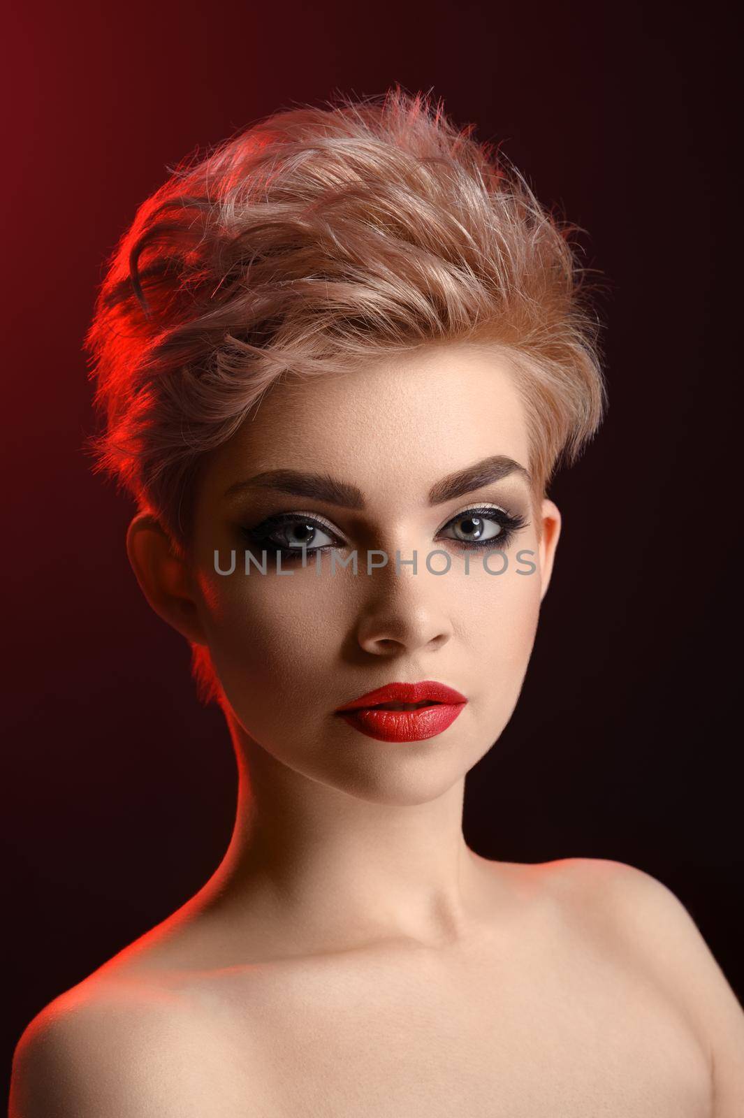 Fierce beauty. Vertical studio portrait of a beautiful young blonde haired woman with smoky eyes and red lips makeup looking confidently to the camera cosmetics visage fashion modeling concept