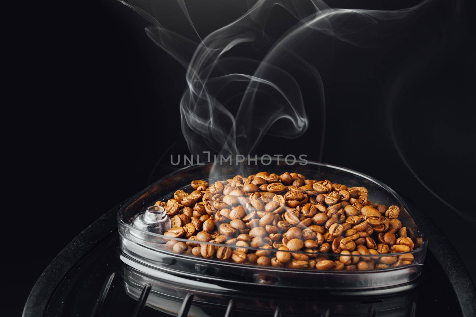 fresh roasted coffee beans with smoke in coffeemaker bean container, close-up view by nikkytok