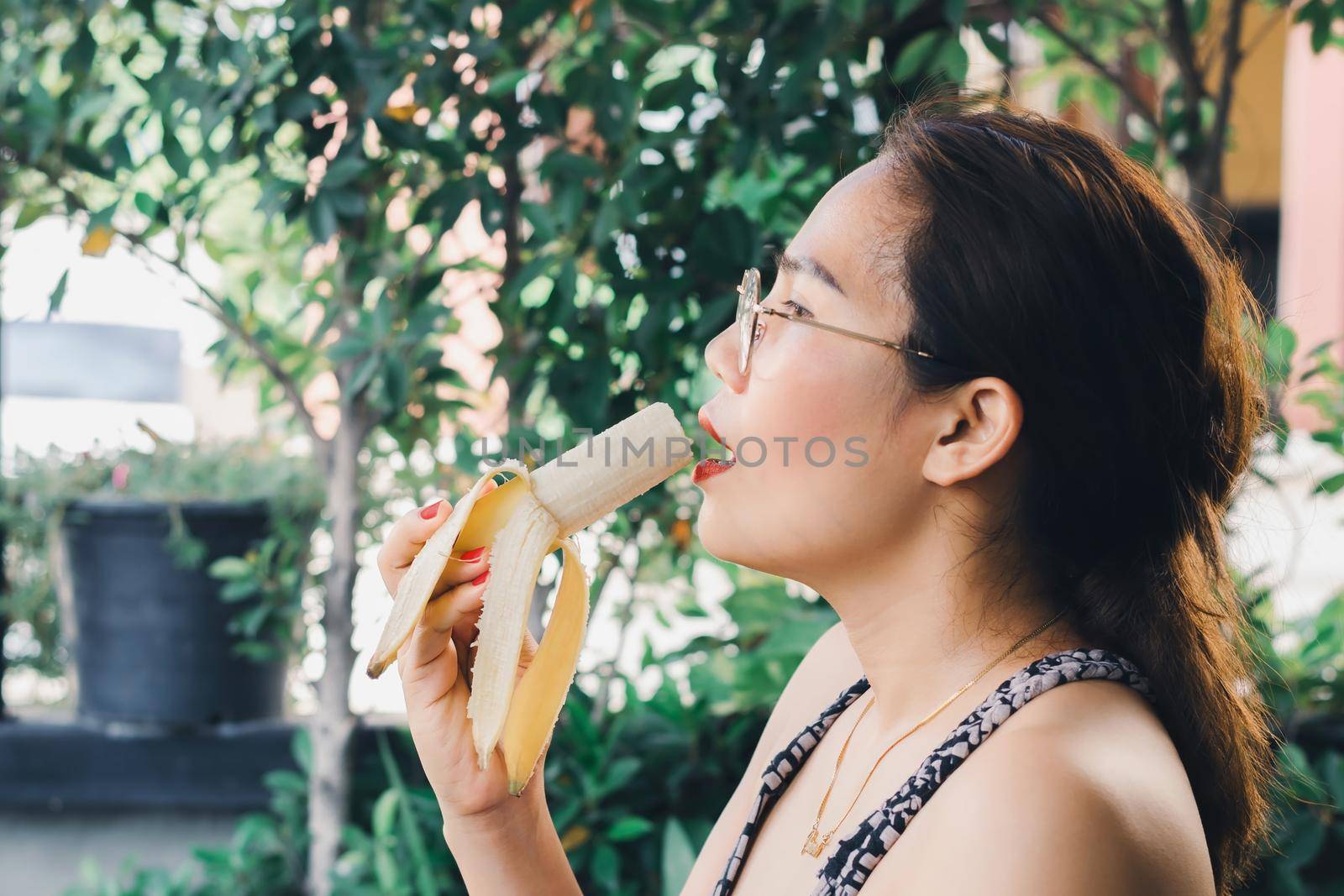 Asian woman in glasses with a red nail polish and a lip stick eating a ripe banana