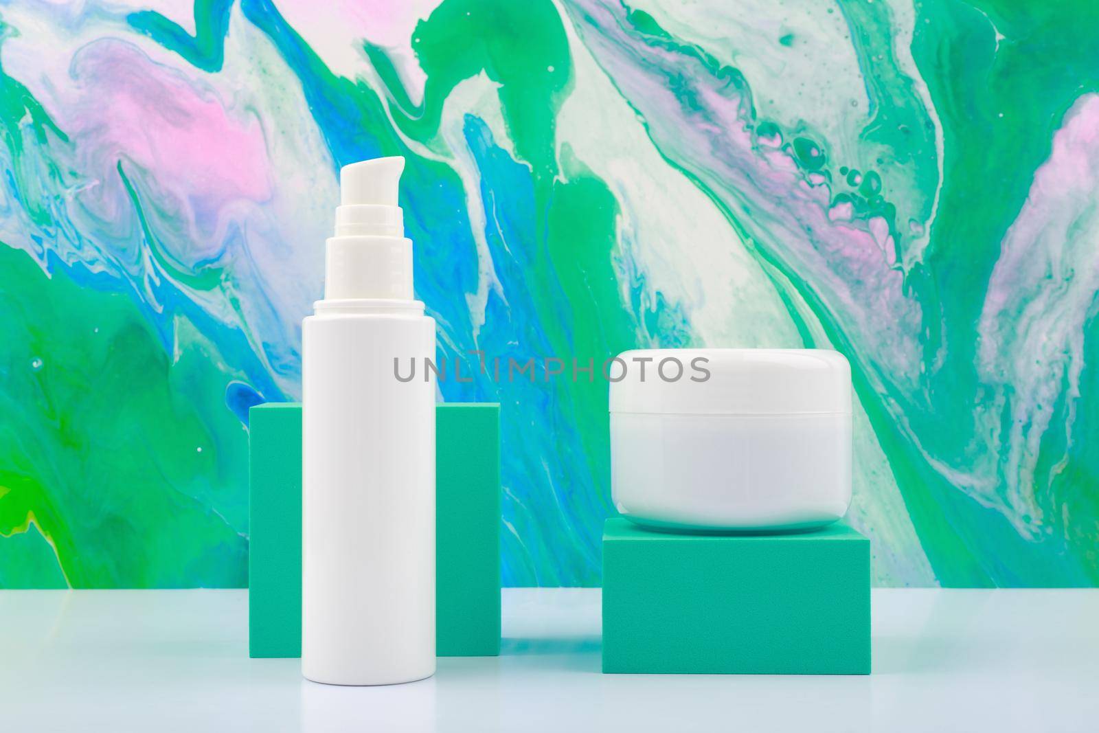 Set of cosmetic bottles with cream, mask, scrub or lotion against trendy marbled background in blue and green tones. Concept of skin care and beauty