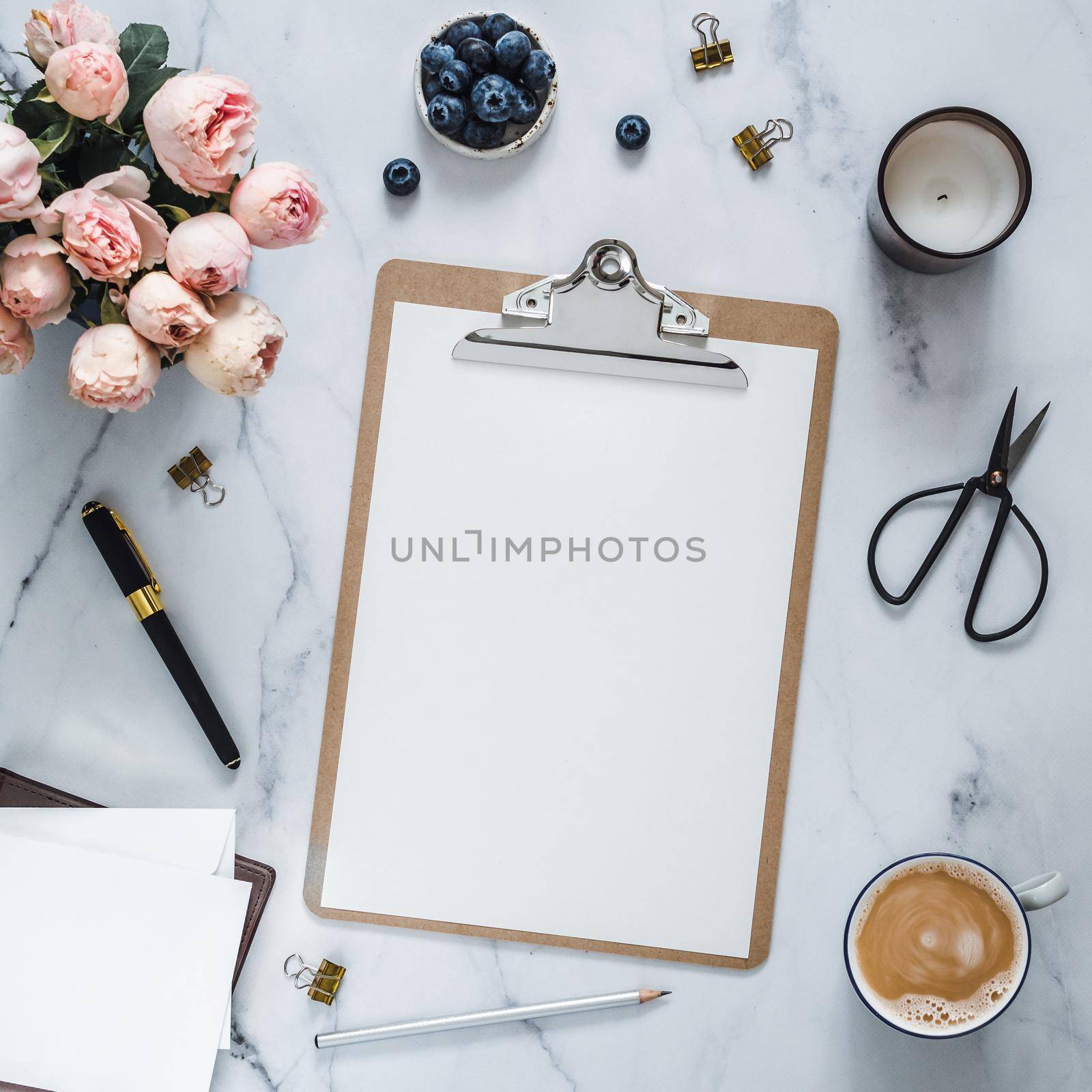 Top view of clipboard with white empty page. Clipboard, flowers, scented candle on white marble. Feminine home office mockup with blank sheet of paper A4 portrait format, copy space. Flat lay