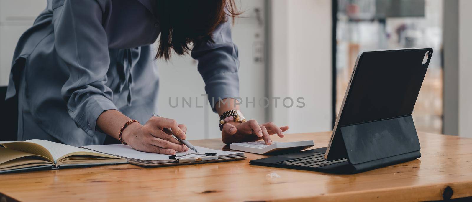Close up of businesswoman or accountant taking note and working on calculator and laptop computer to calculate business data during make note at notepad, accountancy document at office