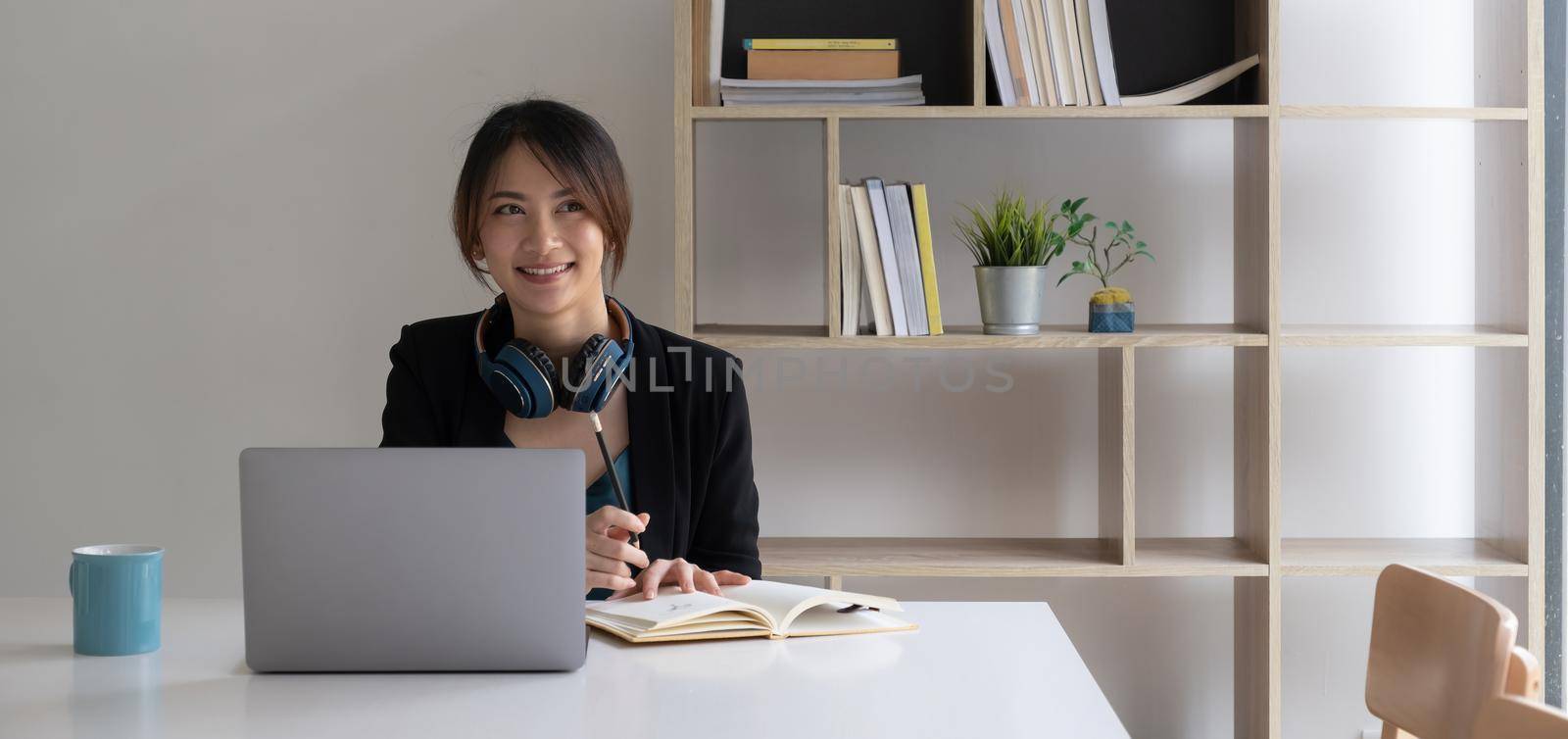 Portrait of a student sitting at her desk at home, studying online with a laptop and writing notes in a notebook