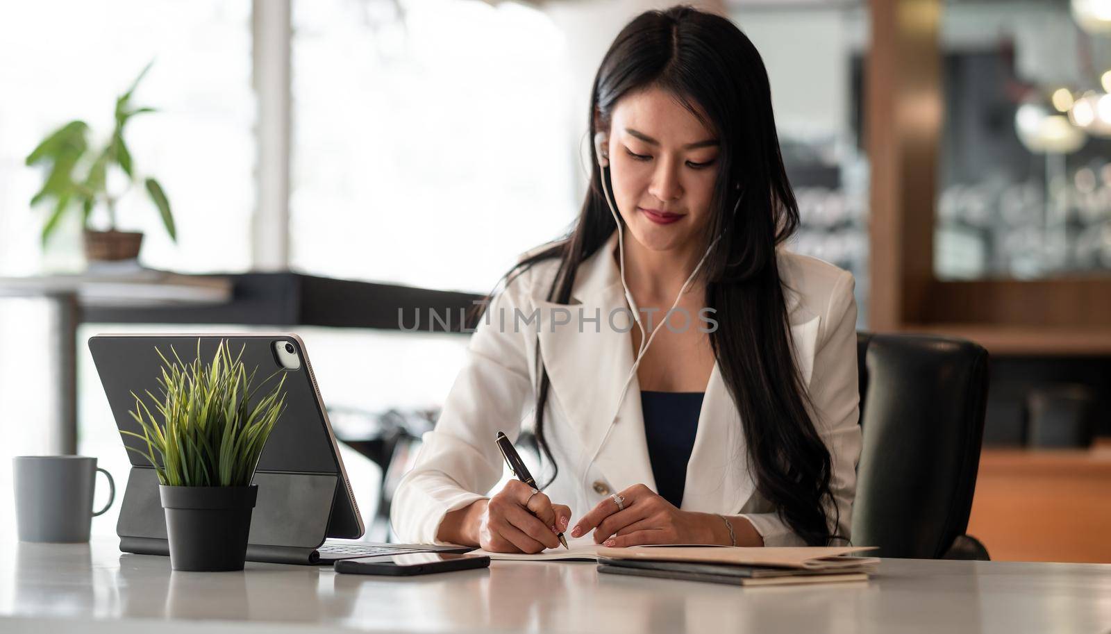 Businesswoman with earbuds for video conference lecture note.woman using tablet webinar video course at home office by nateemee