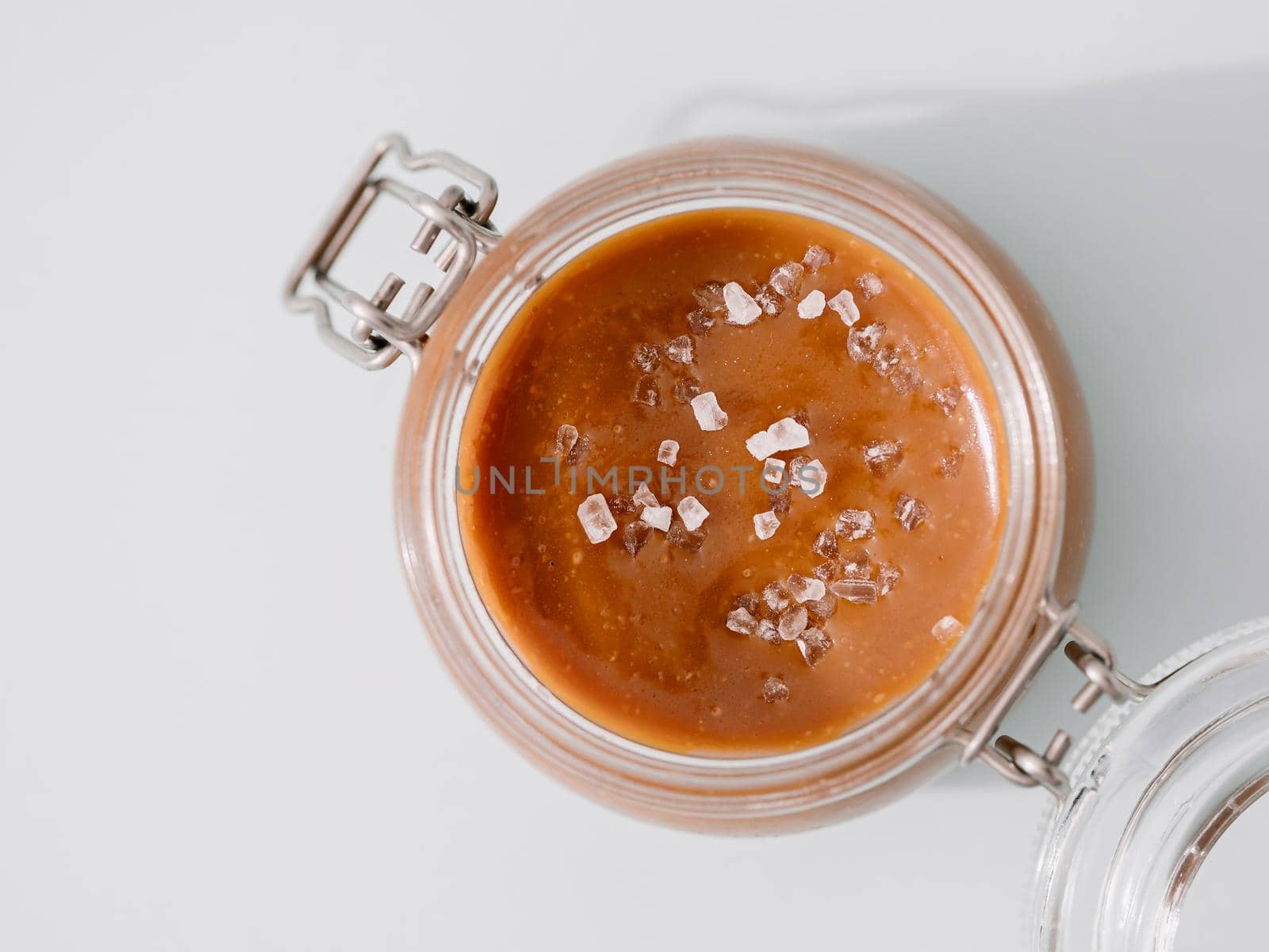 Salted caramel in glass jars, top view. Close up view of delicious brown caramel or condensed milk with sea salt crystalls. Light neutral background